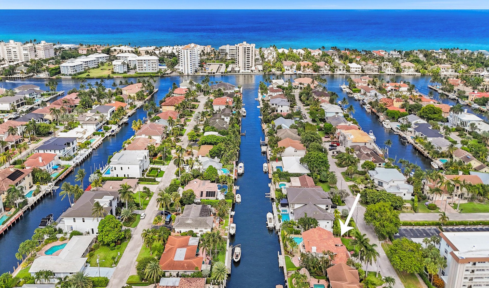 Aerial view of canal-front homes and boats, with the ocean beyond and an arrow pointing to a red-roofed house.