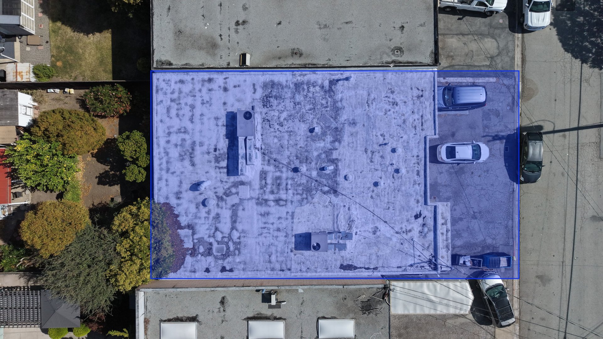 Aerial view of an industrial building outlined in blue, with rooftop equipment and adjacent parking.