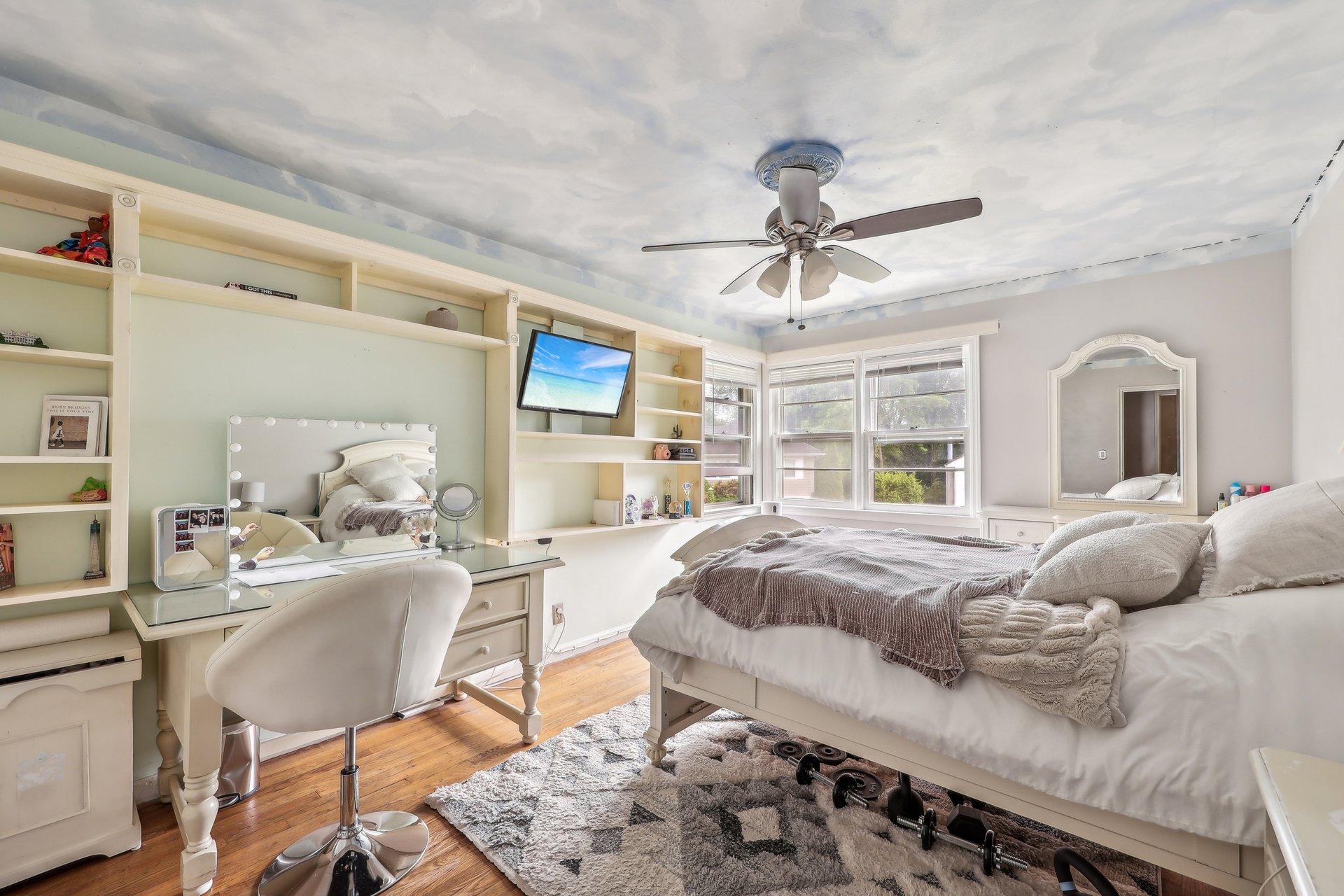 Bedroom with built-in shelving and vanity beside bay windows and a white bed.