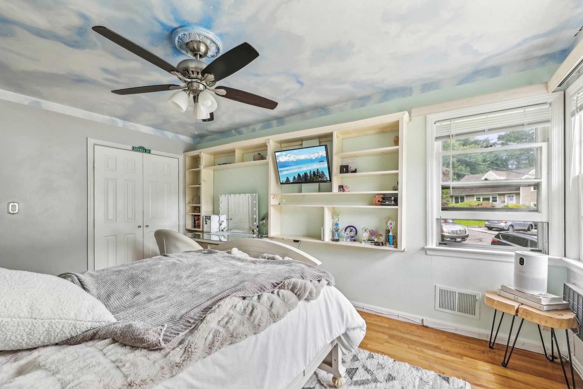 Bedroom with built-in shelving, a sky-painted ceiling, and a large street-facing window.