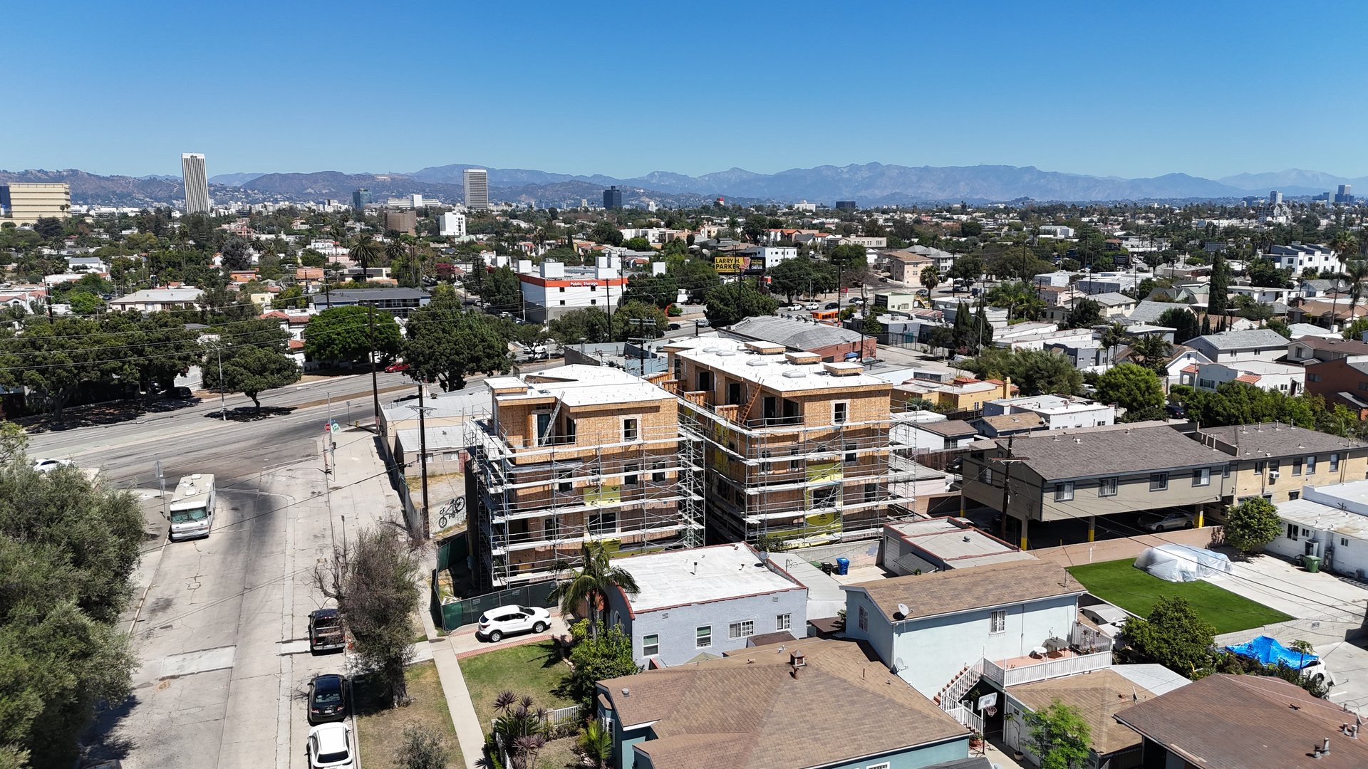 Aerial view of a wood-framed residential building under construction, with scaffolding and mountains in the distance.