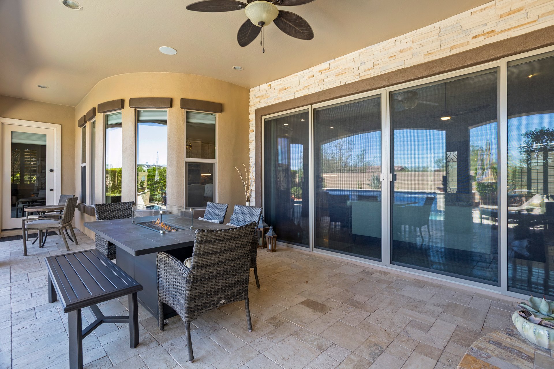 Covered outdoor patio with wicker seating, a fire table, large sliding glass doors, and a view toward the pool area.