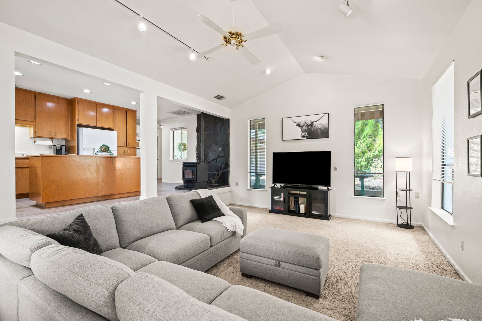 Living room with a gray sectional, open wood-cabinet kitchen, and dark stone fireplace.