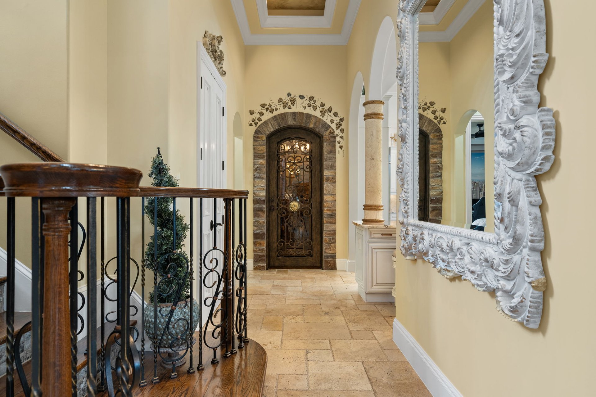 Foyer with a stone-arched wrought-iron door, tiled floor, and ornate white mirror.