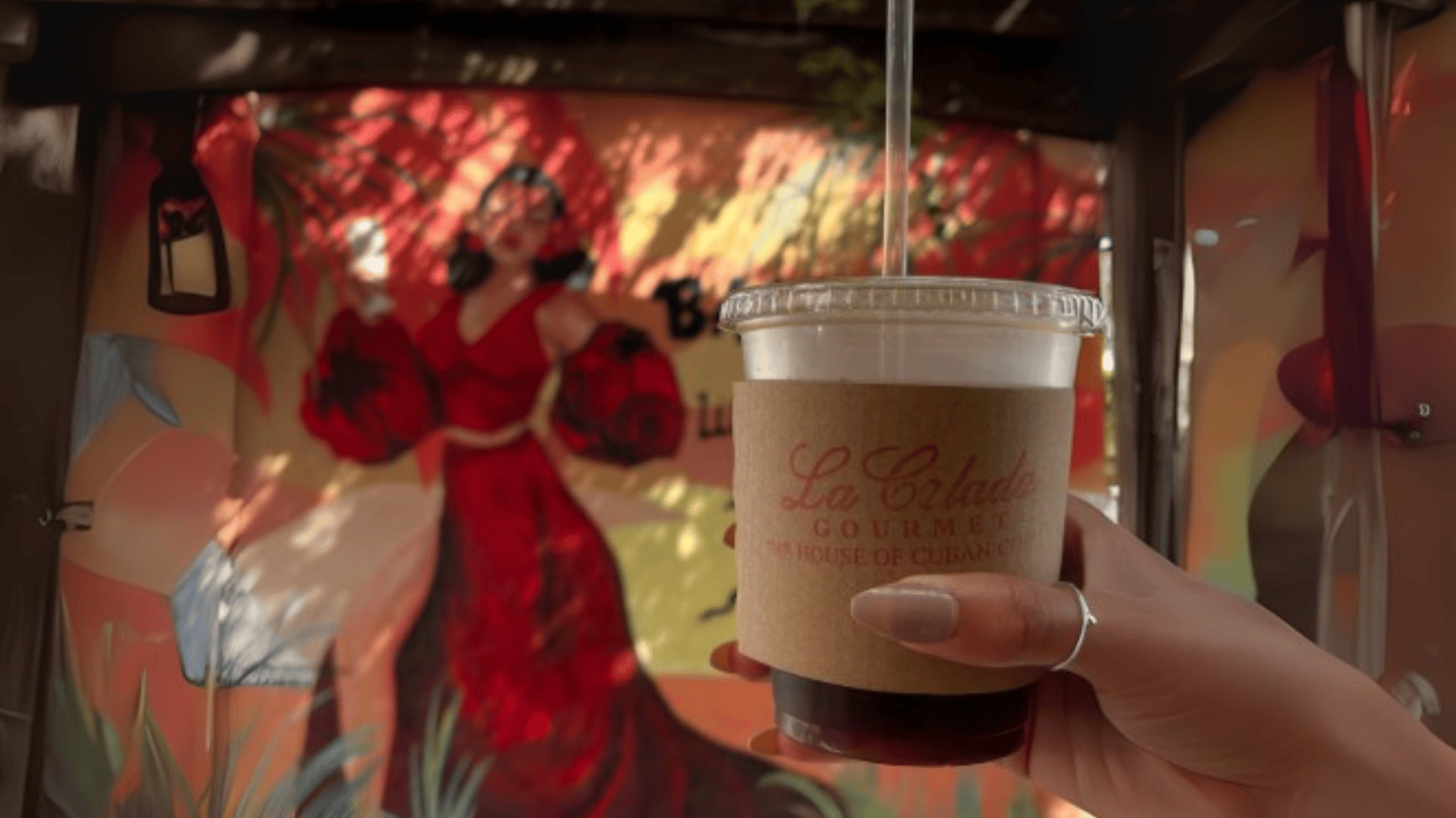 Hand holding La Boheme iced coffee cup with colorful artistic mural background - Miami's vibrant coffee scene by The Edit Real Estate