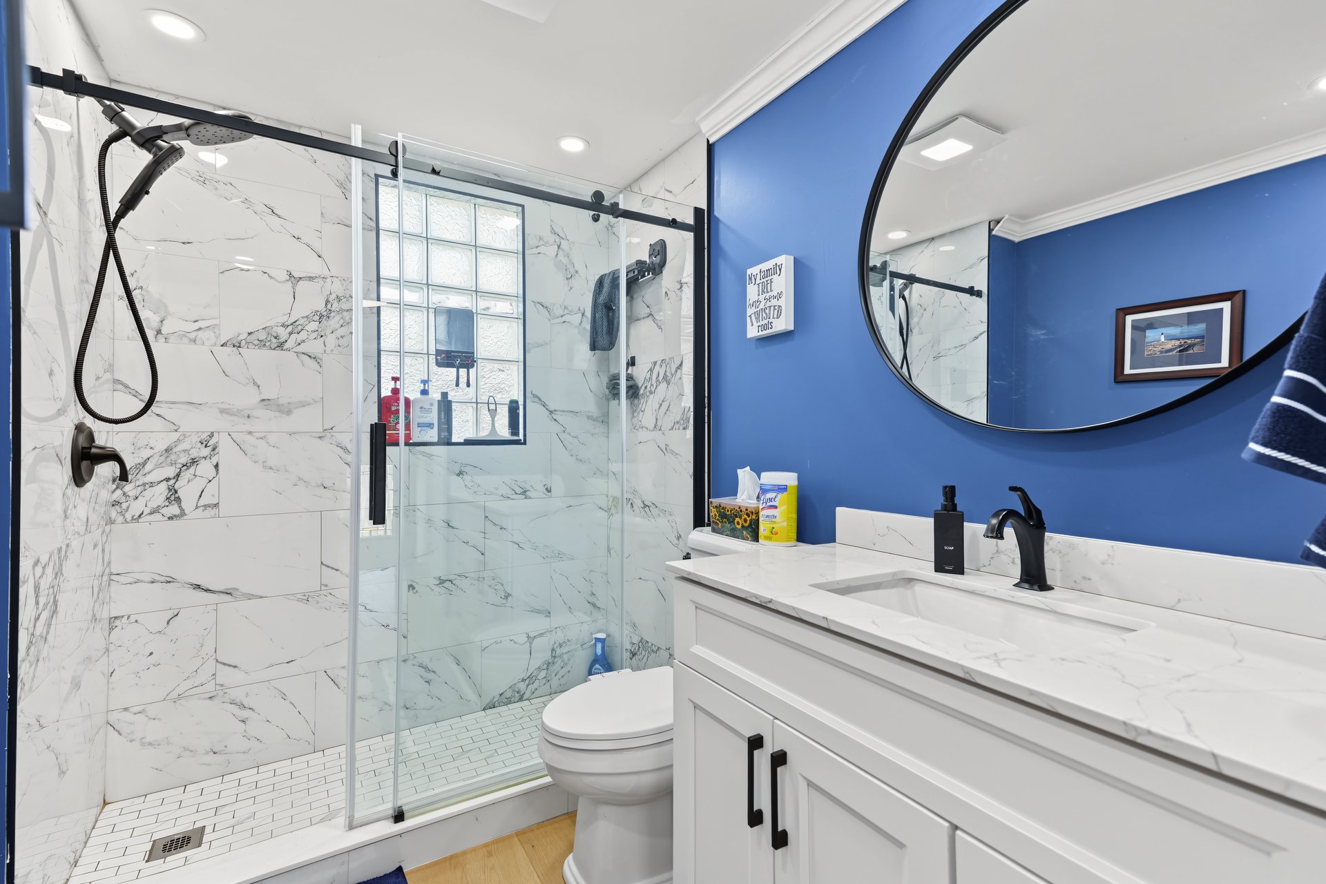 Bathroom with a glass shower, marble-look tile, blue accent wall, and oval mirror.