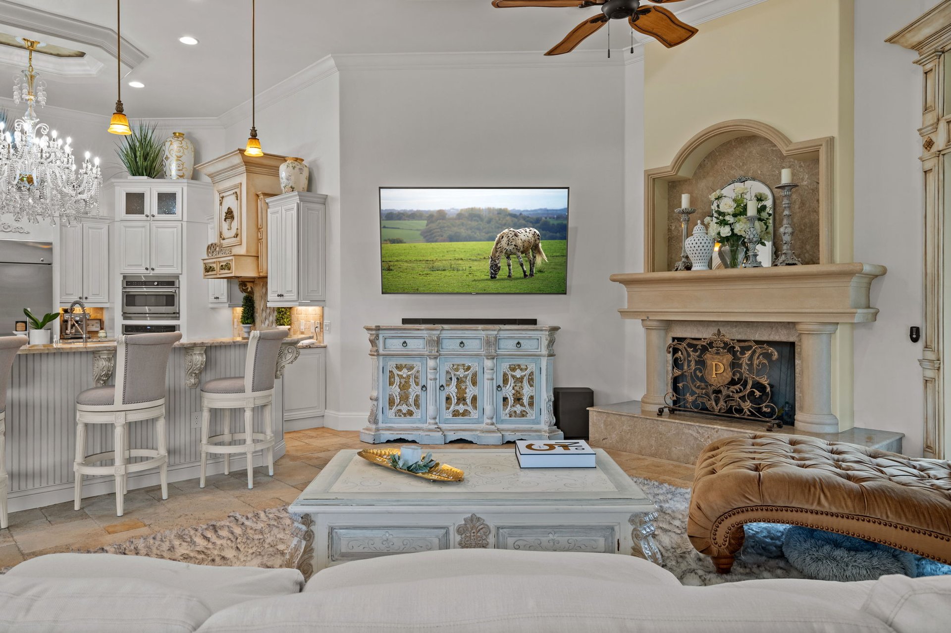 Open-plan living room and kitchen with an ornate stone fireplace and white cabinetry.