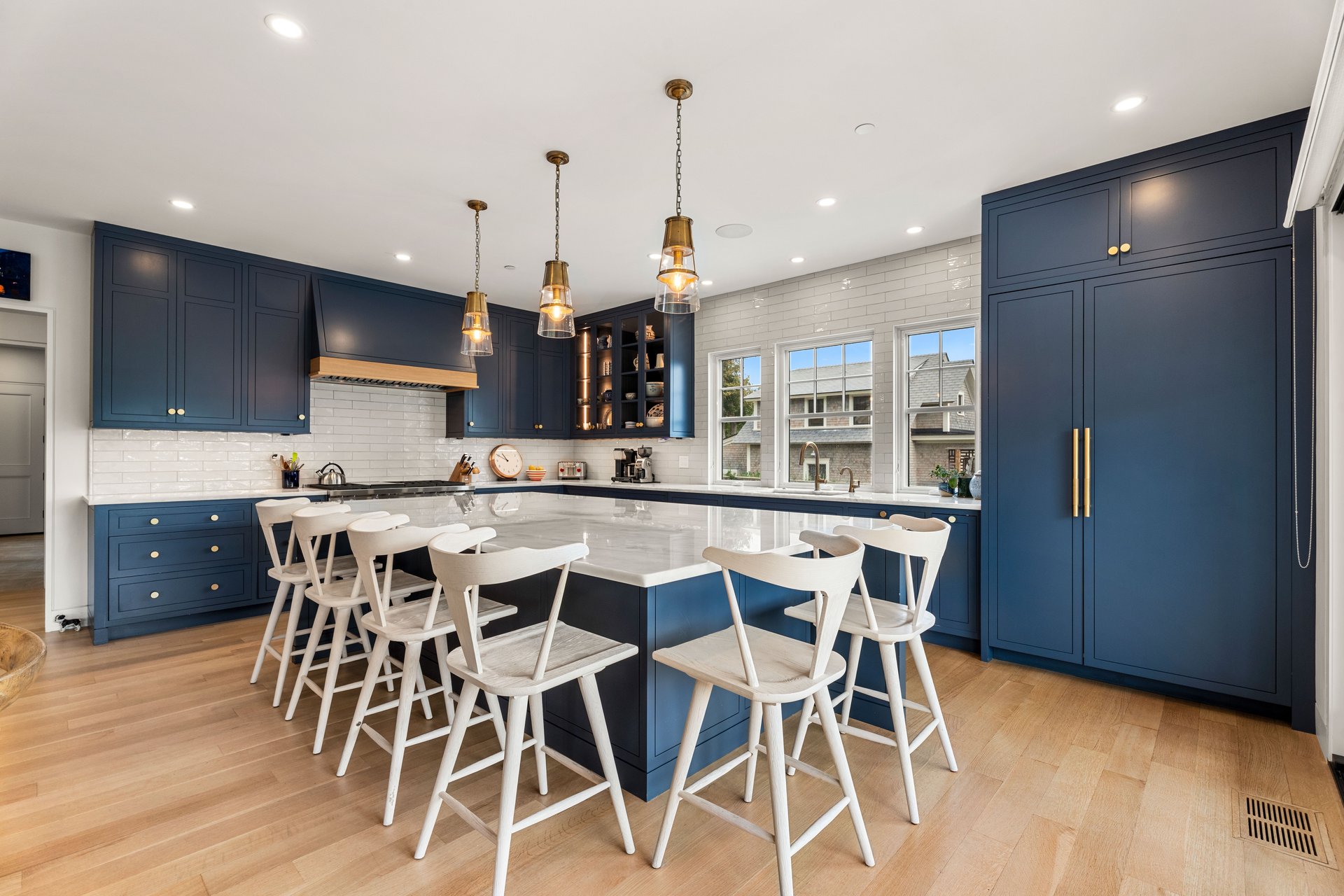 Kitchen with navy cabinetry, a large seating island, white tile backsplash, and pendant lights.