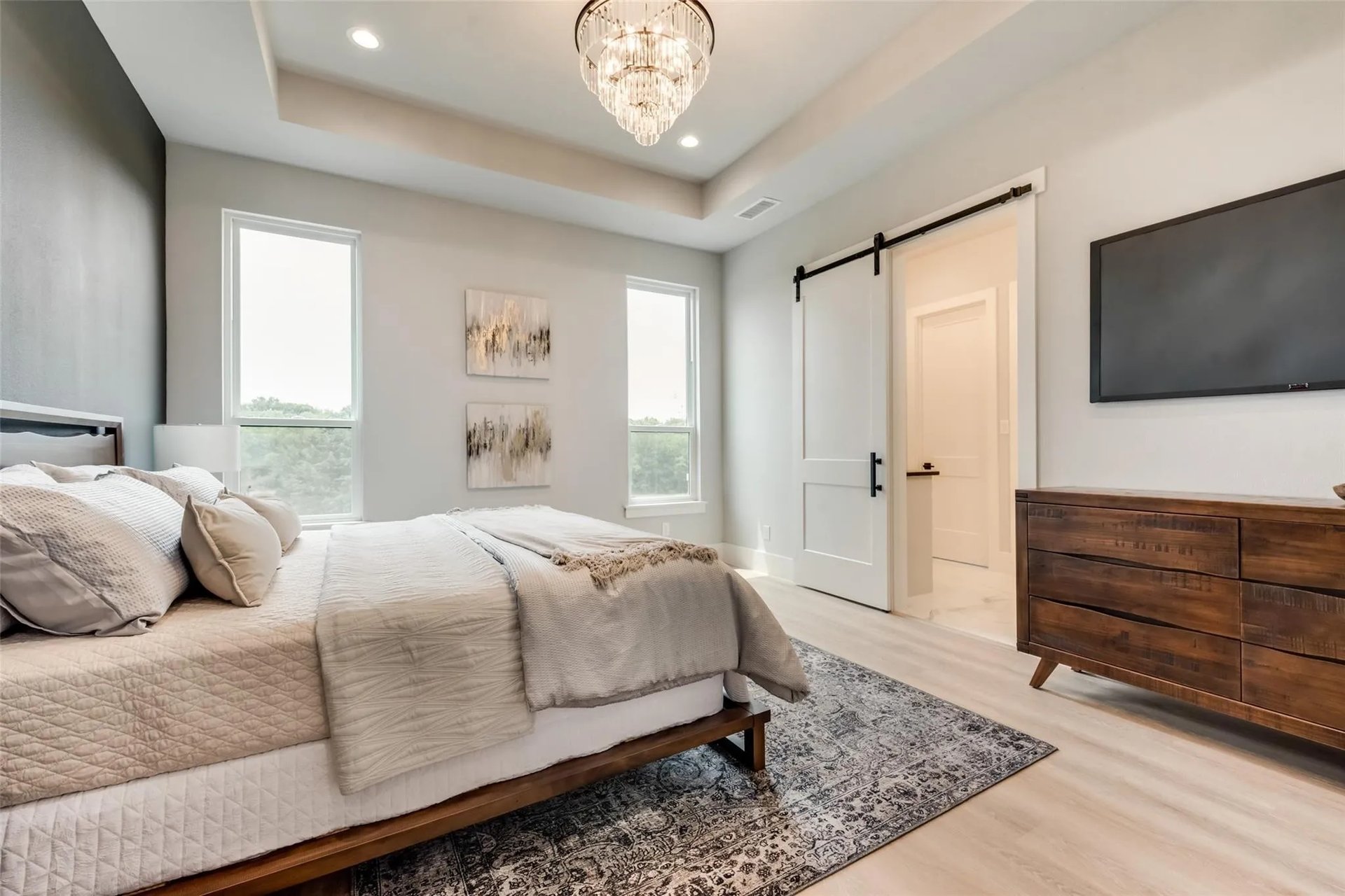 Bedroom with neutral bedding, a crystal chandelier, tall windows, and a sliding barn door.