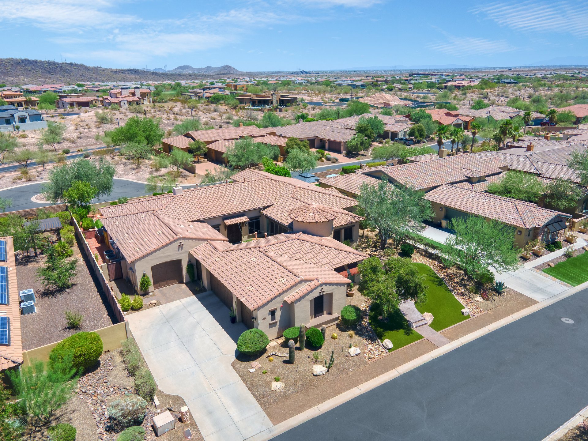 Aerial view of a suburban desert neighborhood with single-story homes, streets, and mountains in the distance.