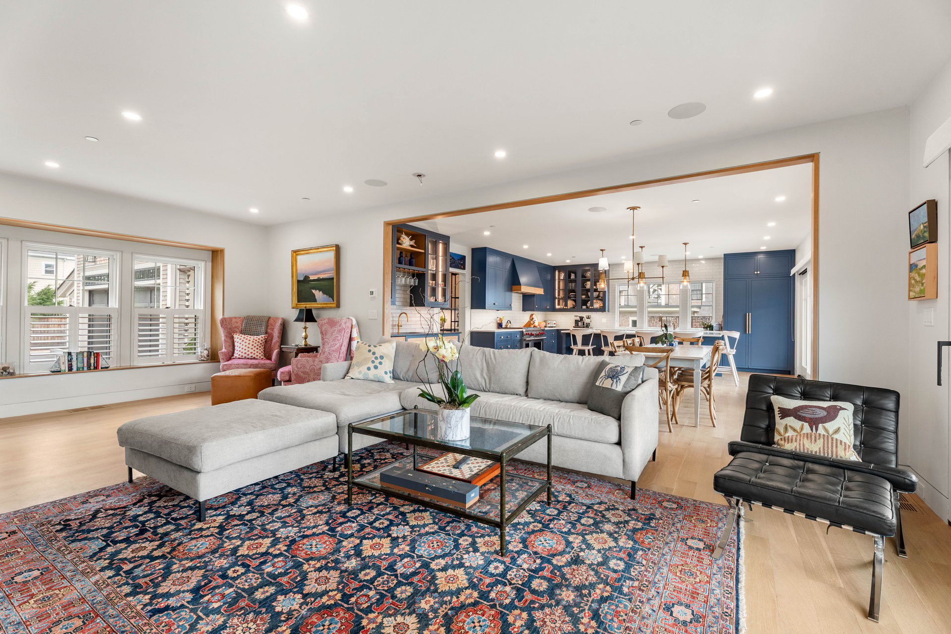 Open-plan living room with a gray sectional, colorful patterned rug, and blue kitchen beyond.