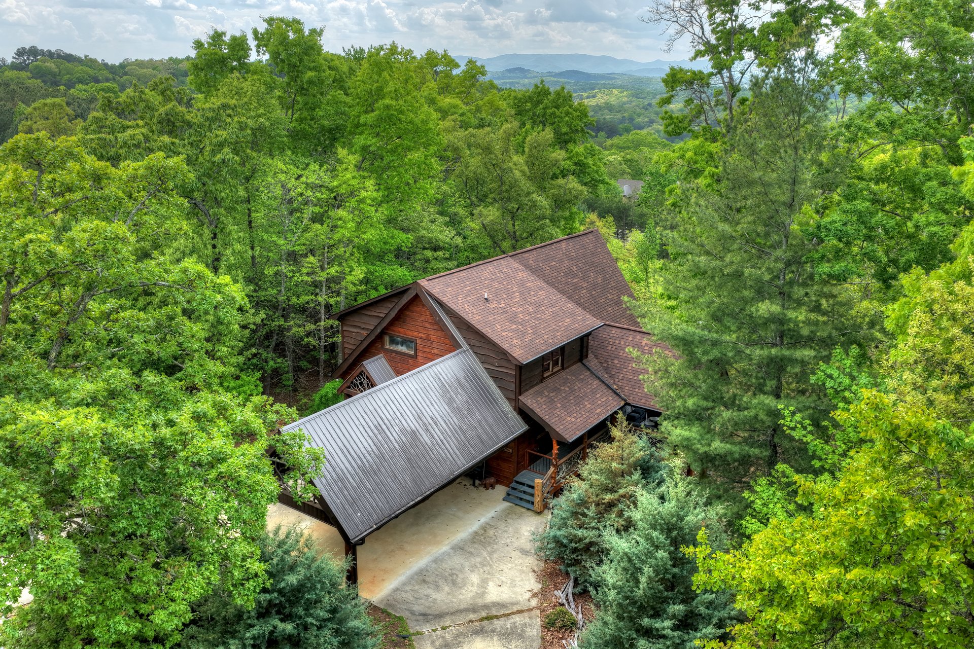 Wooden mountain home nestled in dense forest, with distant mountain ridges beyond the treetops.