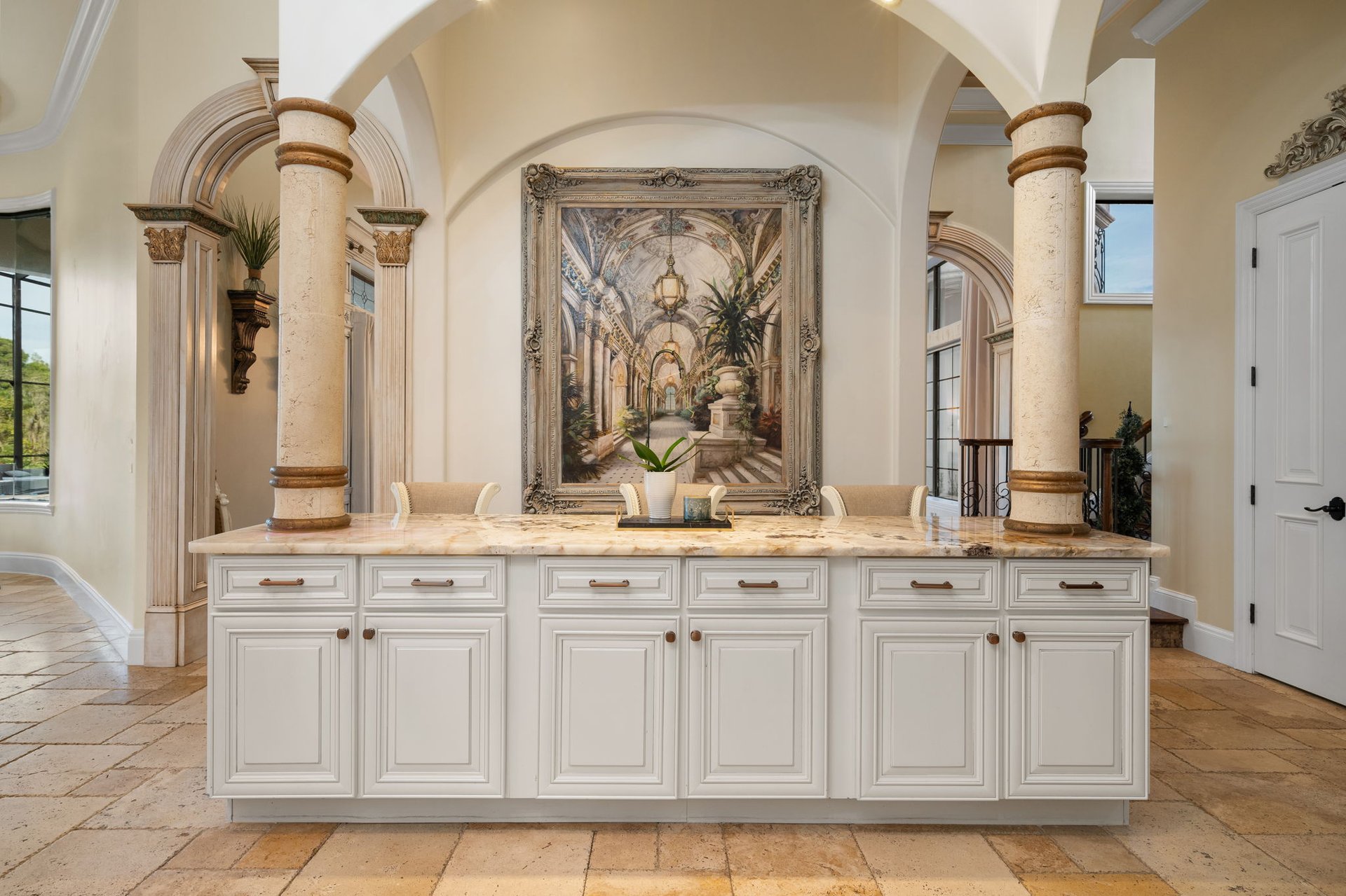 Ornate kitchen with a white paneled island, marble countertop, and stone columns beneath arches.