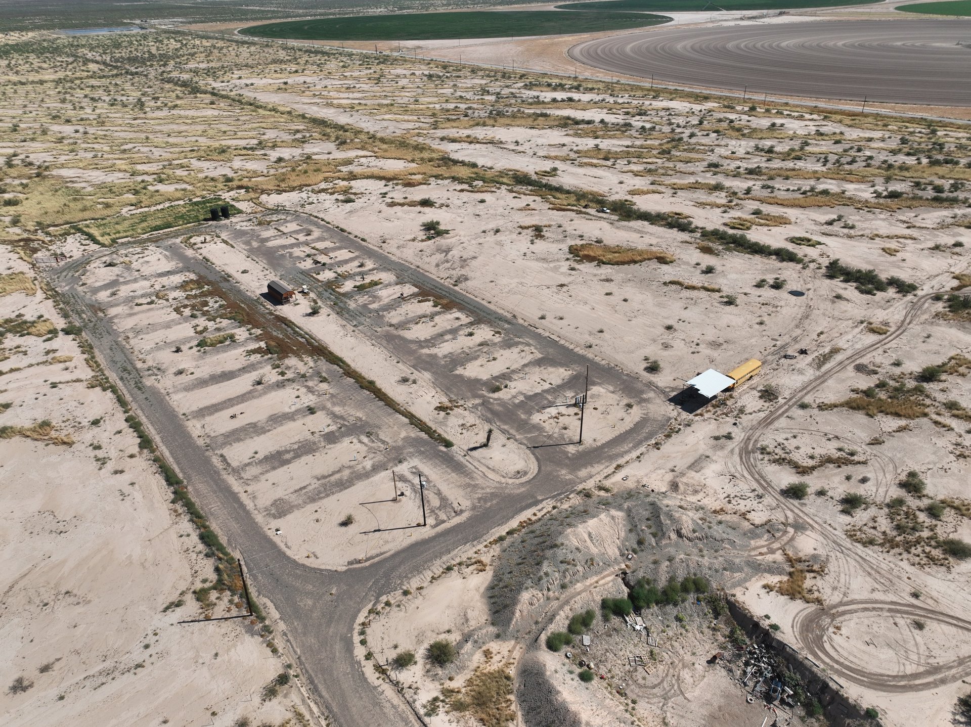 Aerial view of a sandy property with paved roads, cleared pads, and a small white-roofed structure.