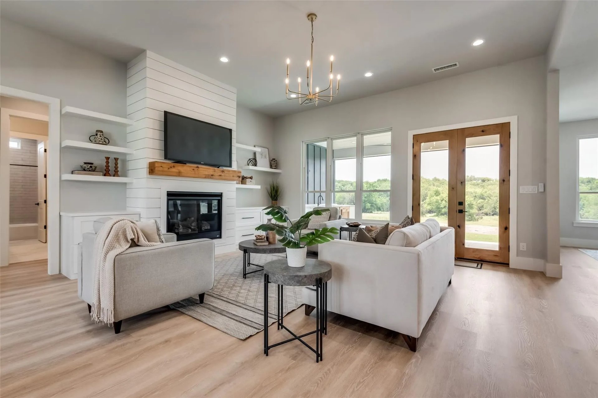 Staged living room with a shiplap fireplace, white sofas, and windows overlooking green countryside.