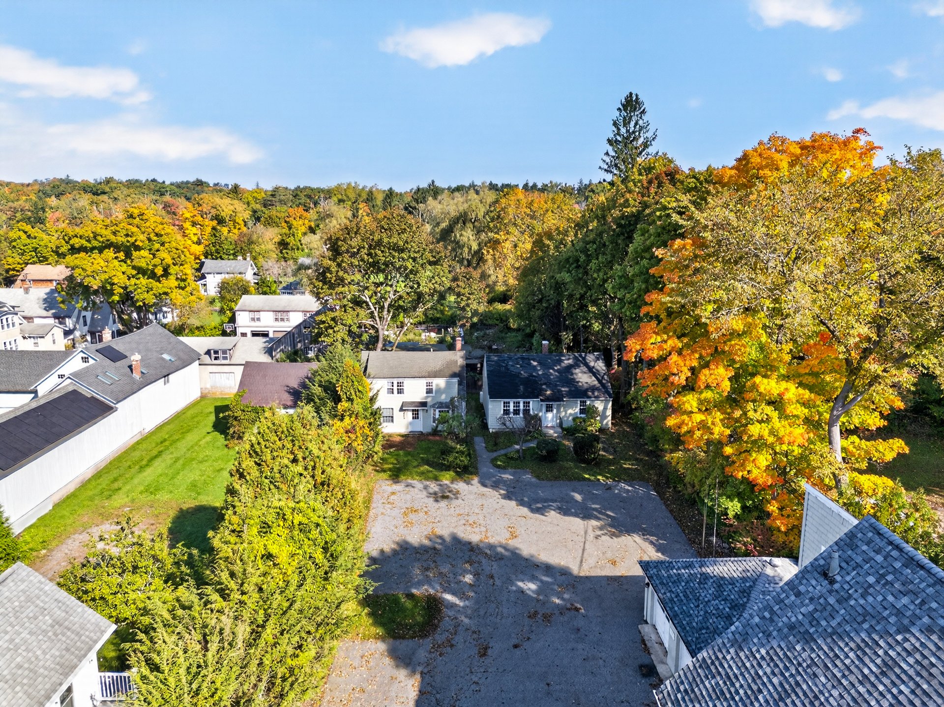 Aerial view of homes around a large paved parking area, framed by colorful autumn trees.
