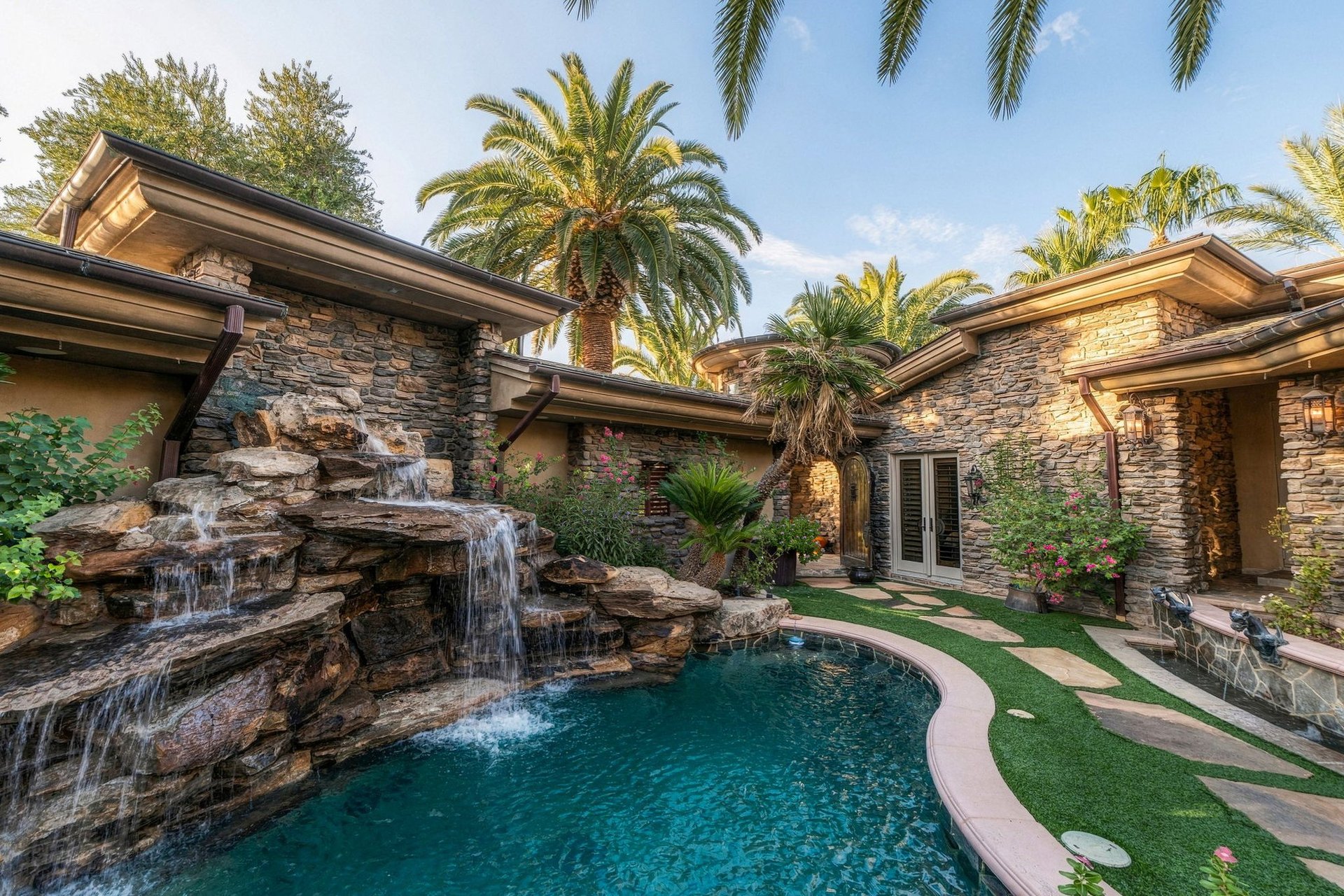 Lagoon-style pool with a rock waterfall and lush landscaping at a luxury home on Foothills Village Drive in MacDonald Highlands, Henderson NV
