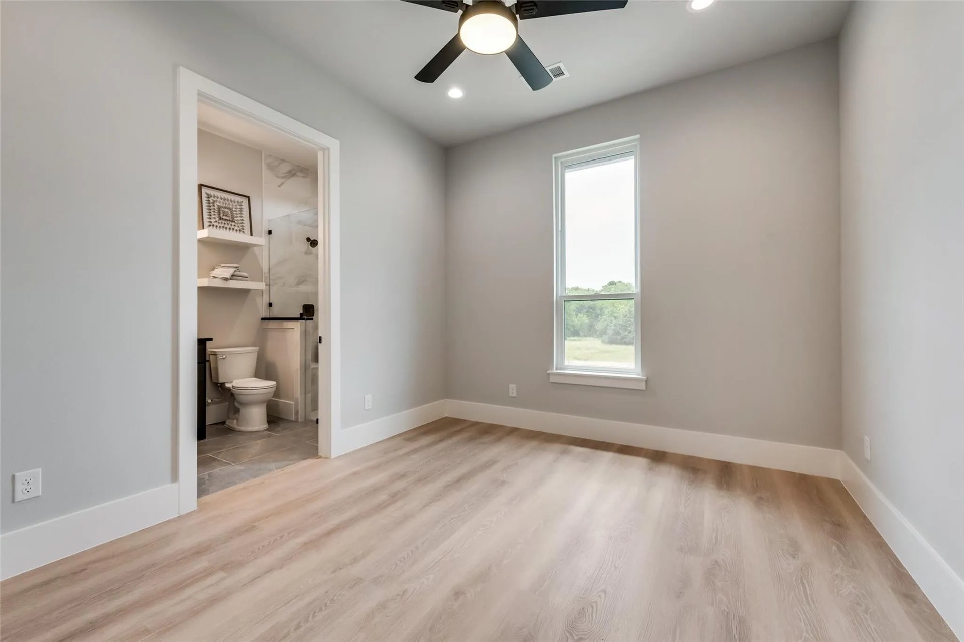 Empty bedroom with light wood floors, a ceiling fan, and an attached bathroom.