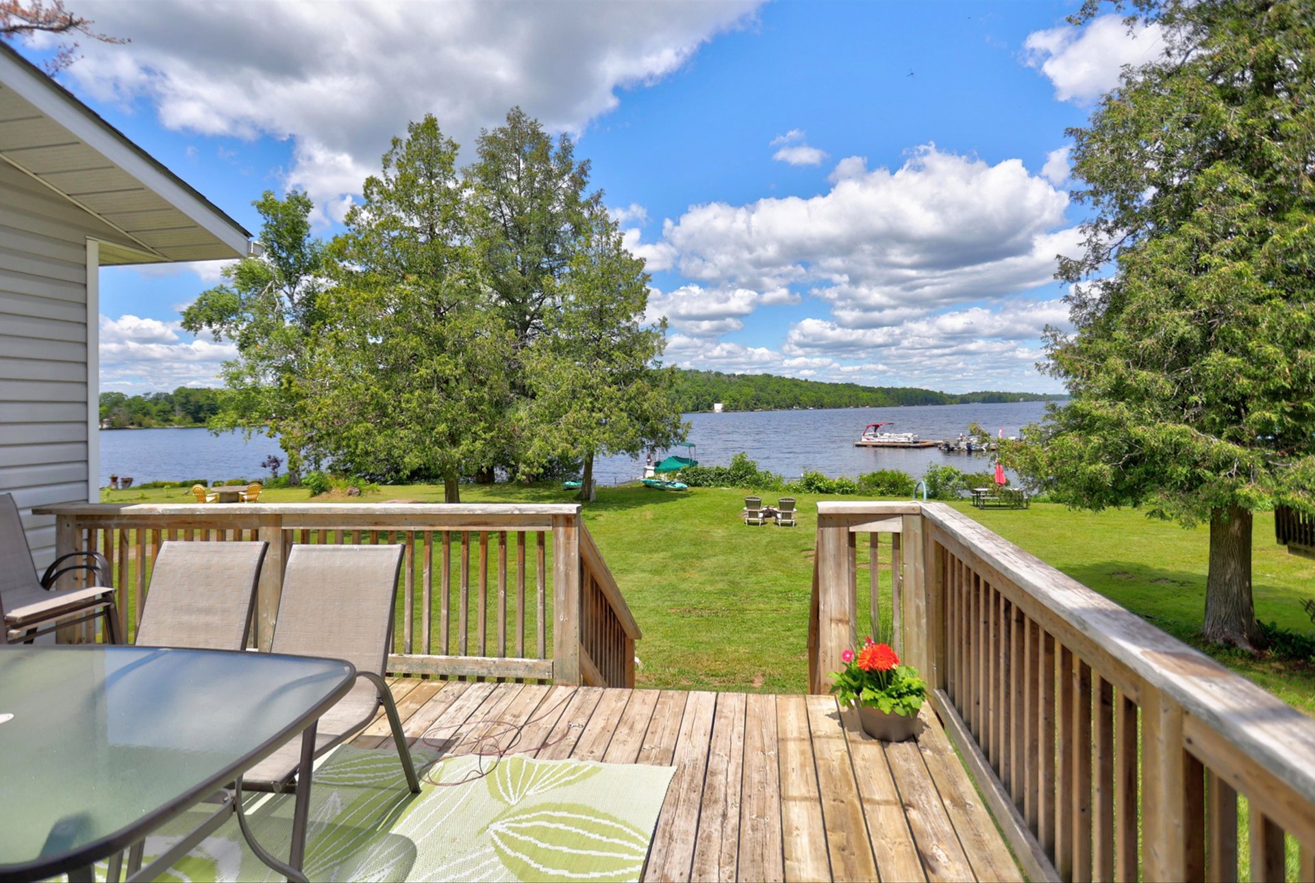 Wooden deck overlooking a lawn and lake, with a dock and boat offshore.