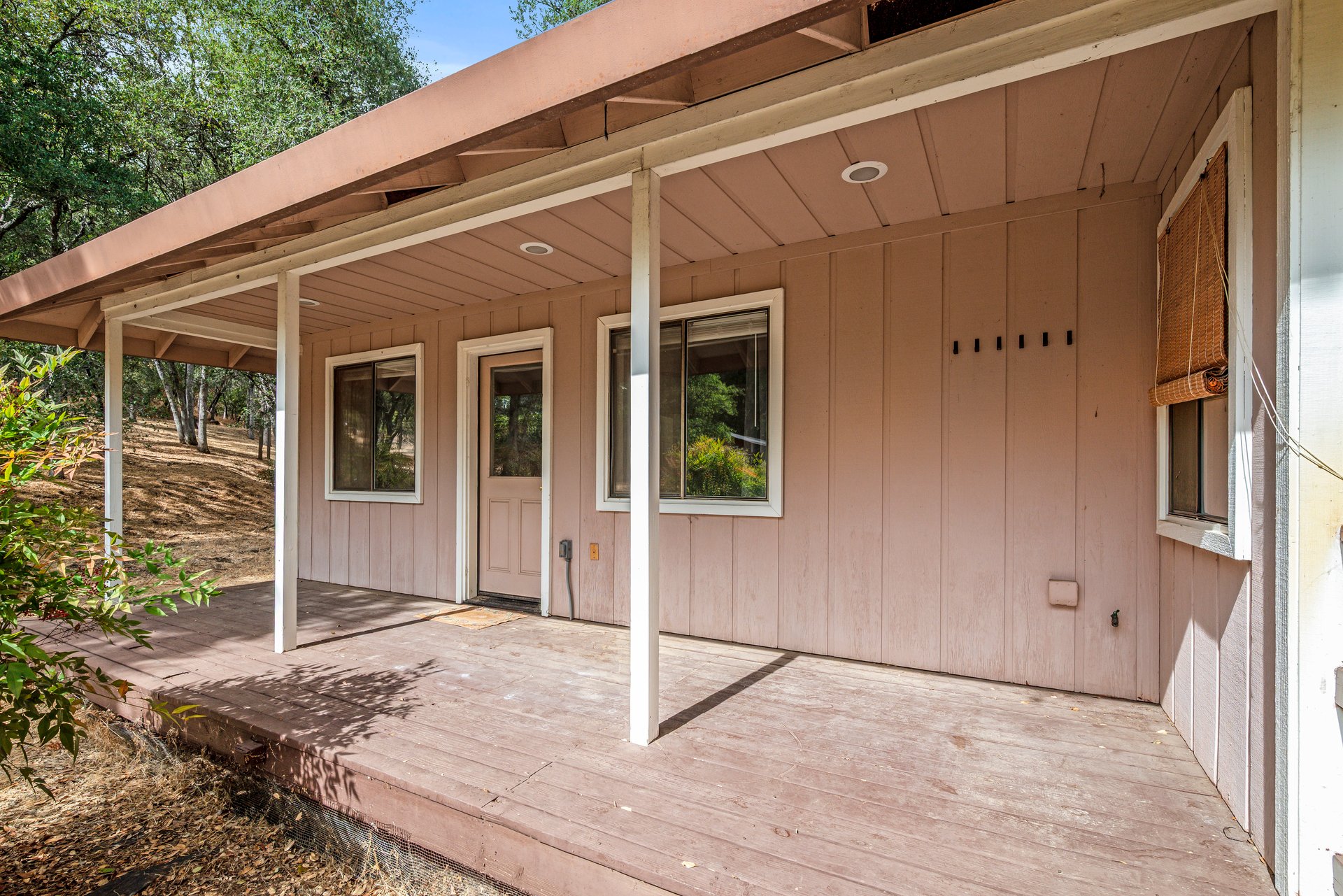Covered wooden porch with pink siding, a central door, and windows overlooking a wooded yard.