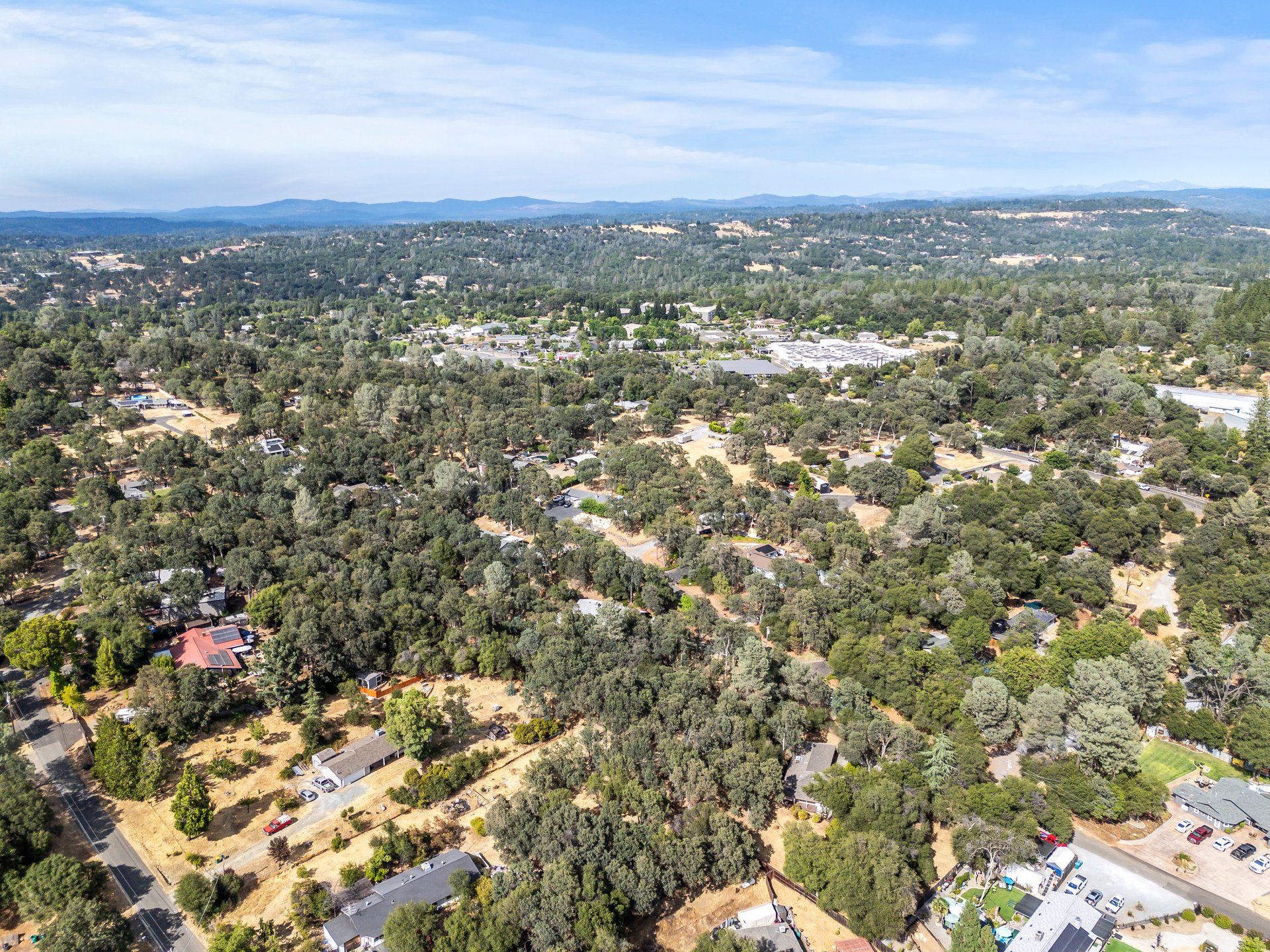 Aerial view of a wooded neighborhood with scattered homes and distant hills.