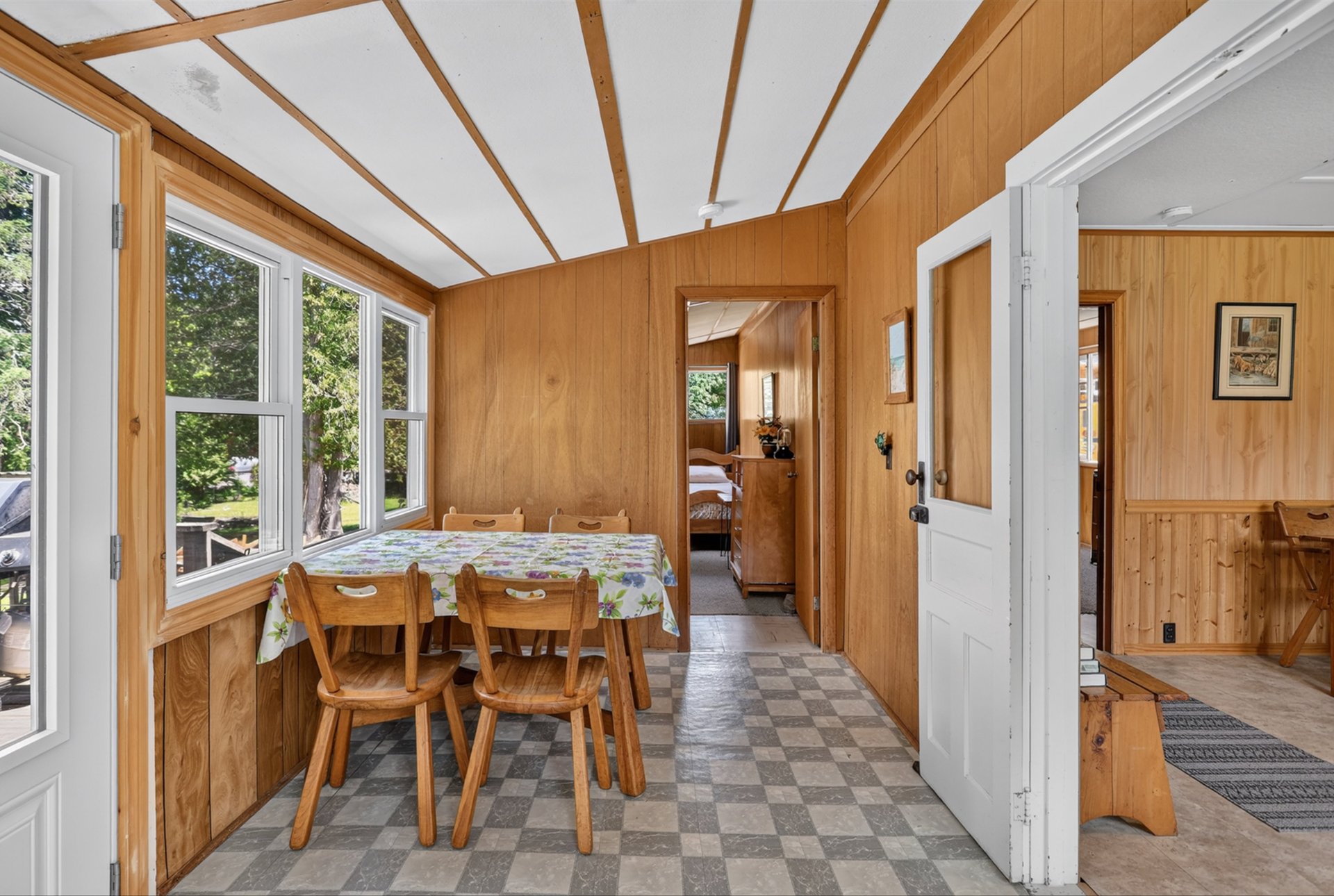 Dining area with wood-paneled walls, a checkered floor, and a table beside large windows.