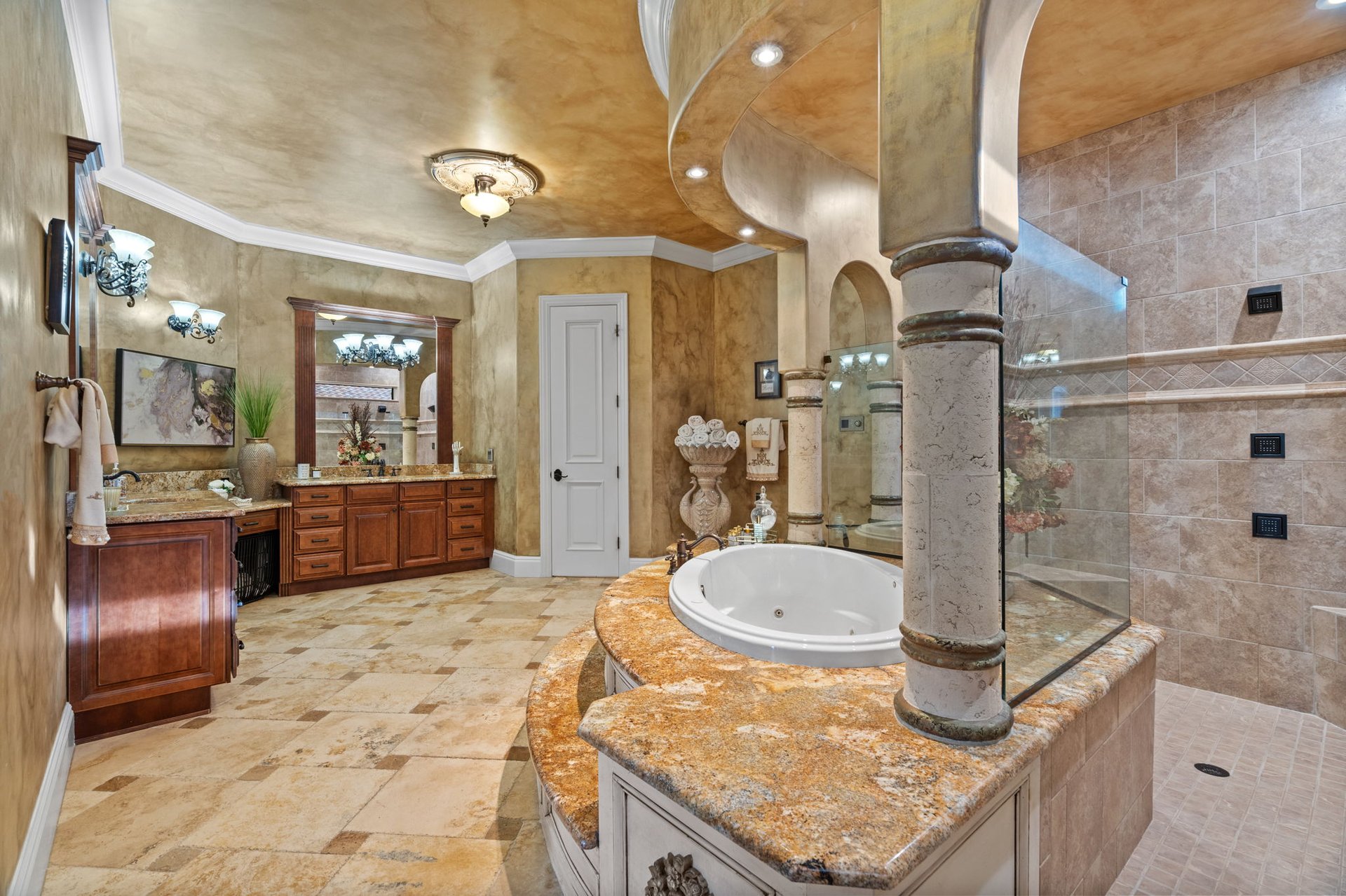 Ornate bathroom with a soaking tub, glass shower, and dual wood vanities.