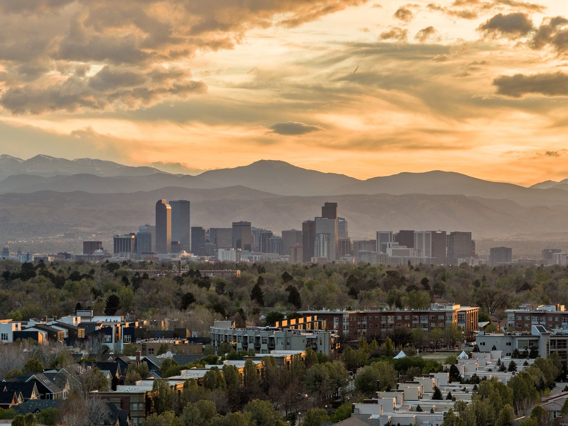 Denver skyline and residential neighborhood with the Rocky Mountains in the distance at sunset.