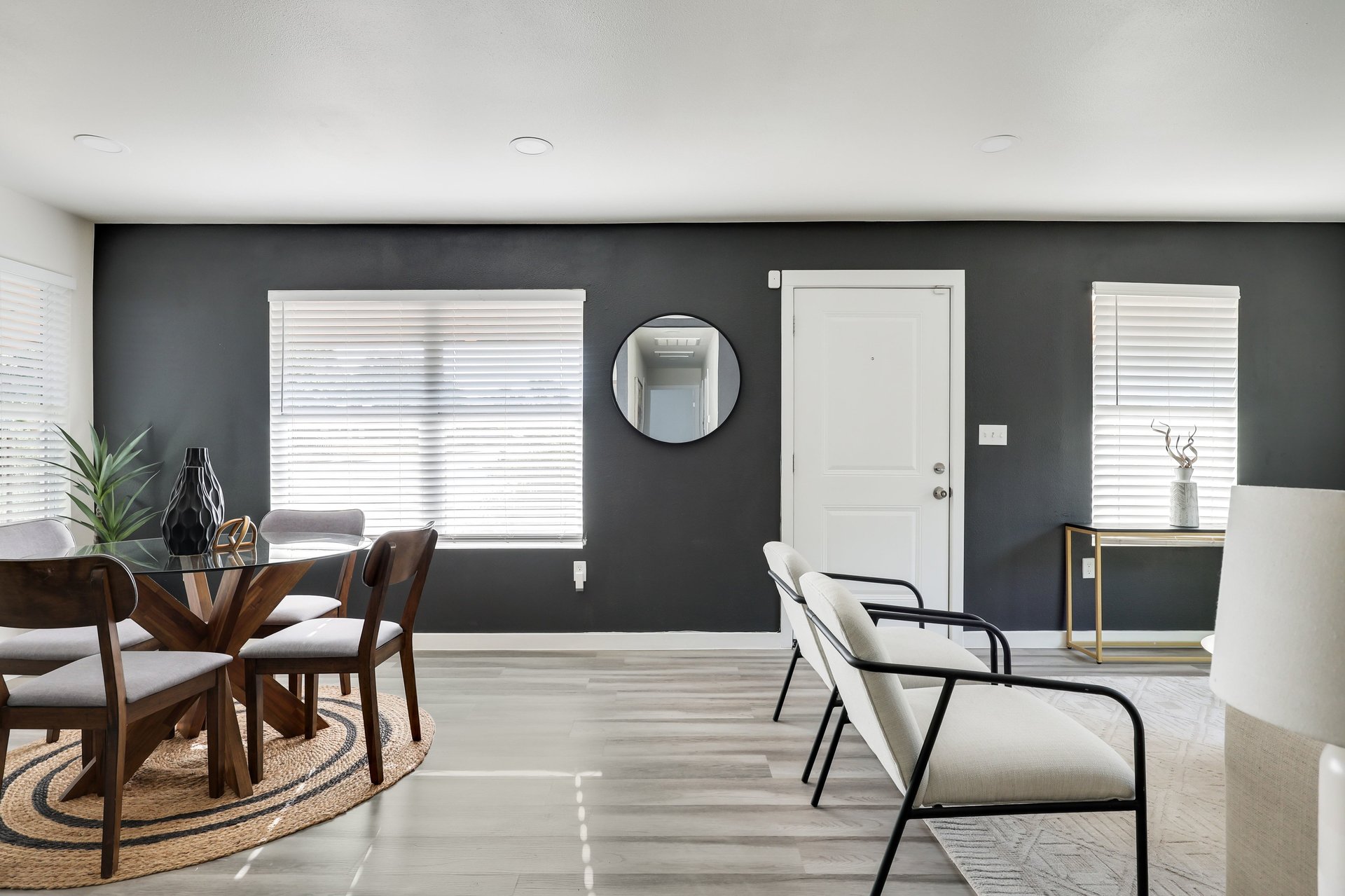 Furnished dining and sitting area with a charcoal accent wall, white front door, and large windows.