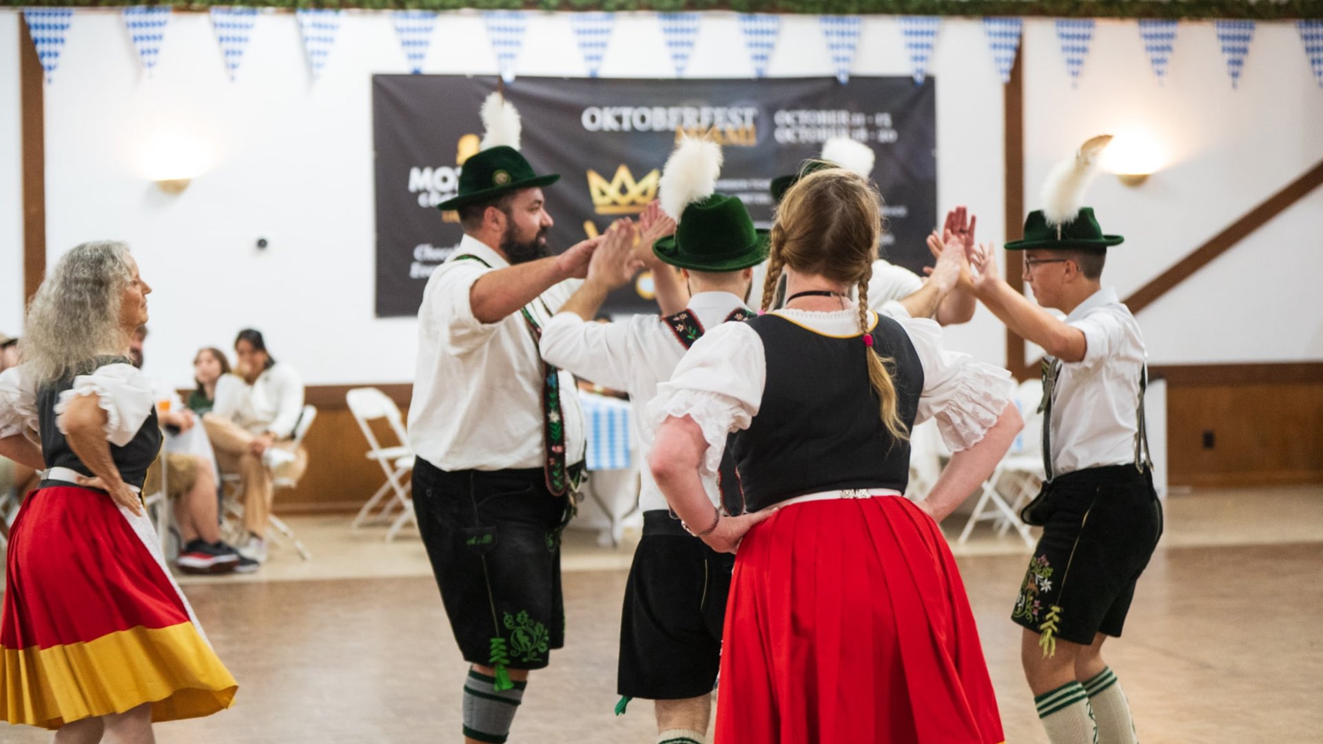 Oktoberfest Miami dancers in traditional German costumes performing Bavarian folk dance with blue and white decorations in background