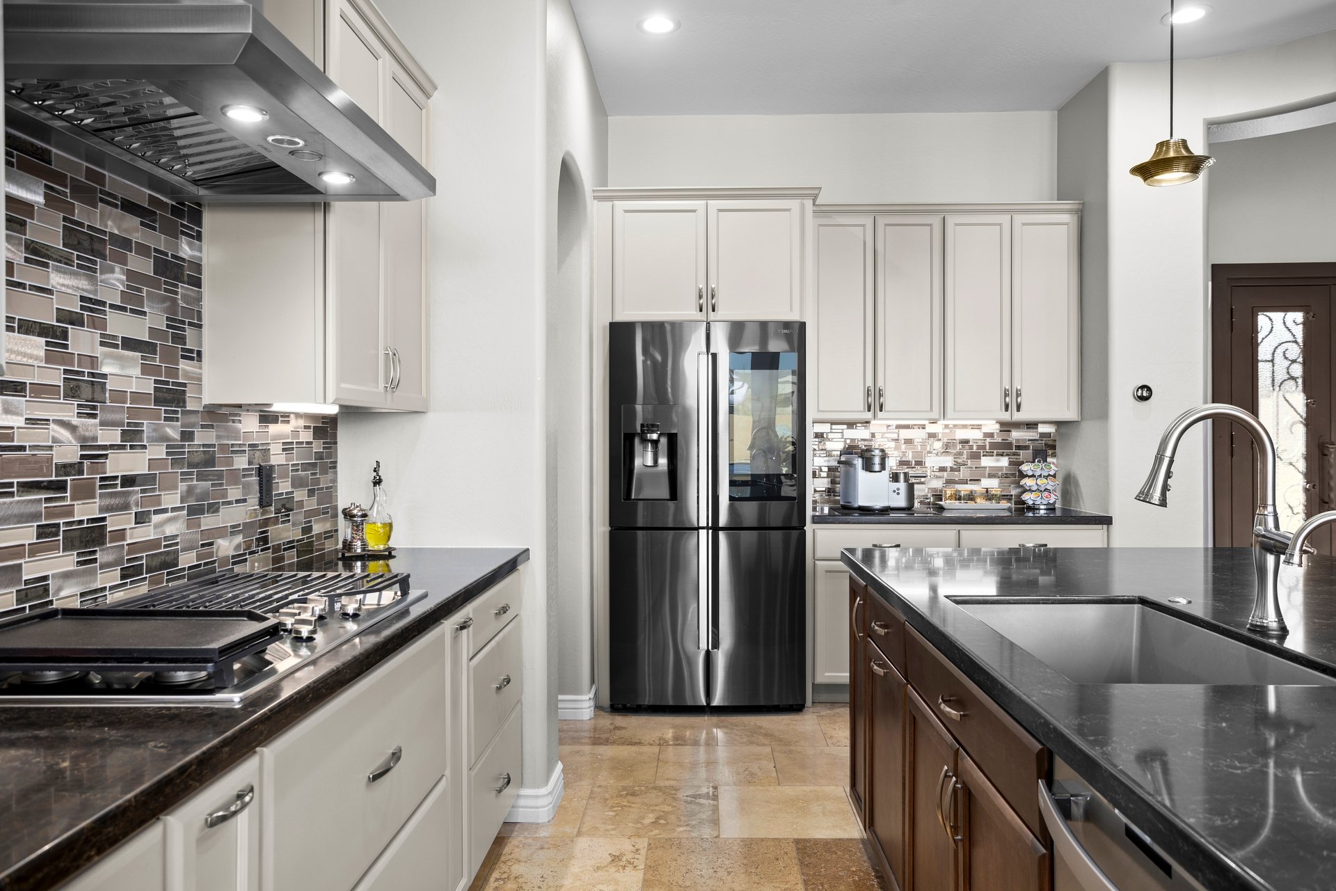 Modern kitchen with black countertops, white cabinets, stainless steel refrigerator, mosaic tile backsplash, and island sink.