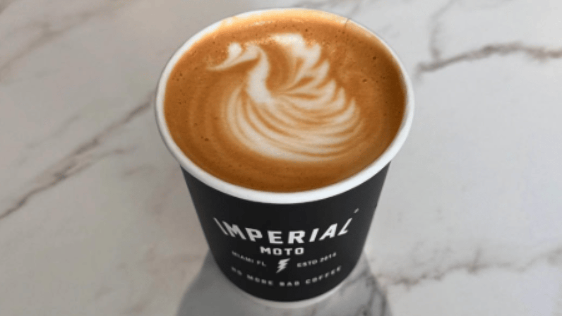 Imperial Moto coffee cup with elegant swan latte art design - Miami specialty coffee shop featured by The Edit Real Estate