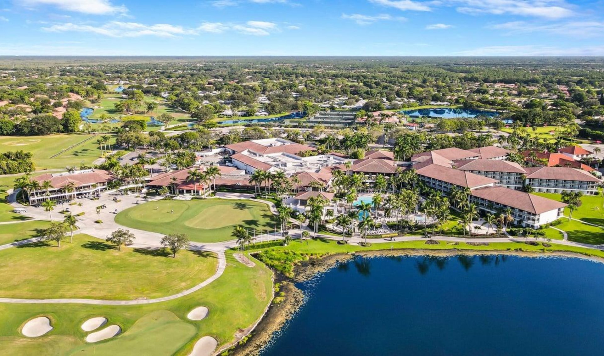 Aerial view of a golf course community with red-roofed buildings and a lake.