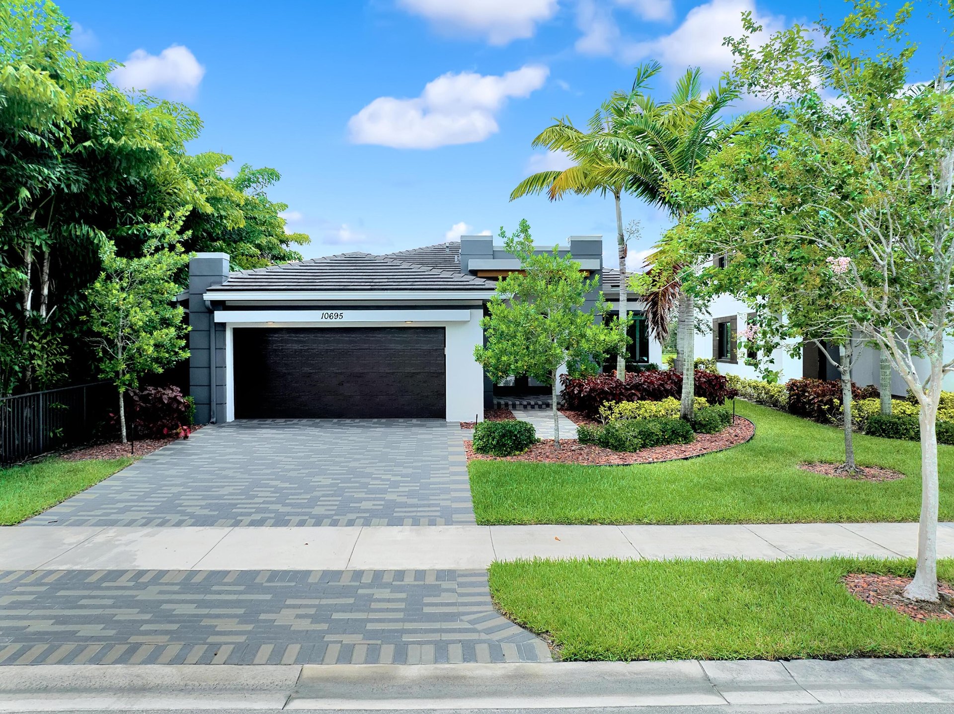 Modern home with a dark double garage, patterned paver driveway, and tropical landscaping.