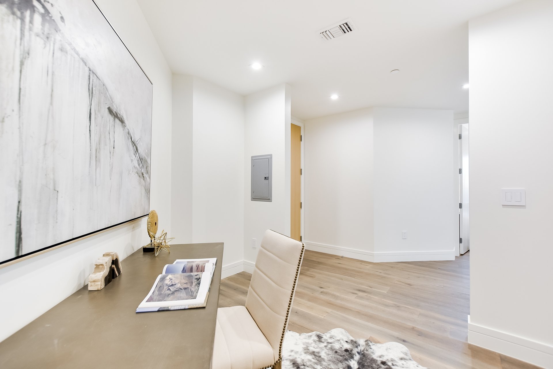 Modern workspace with a taupe desk, cream chair, abstract artwork, and light wood floors.