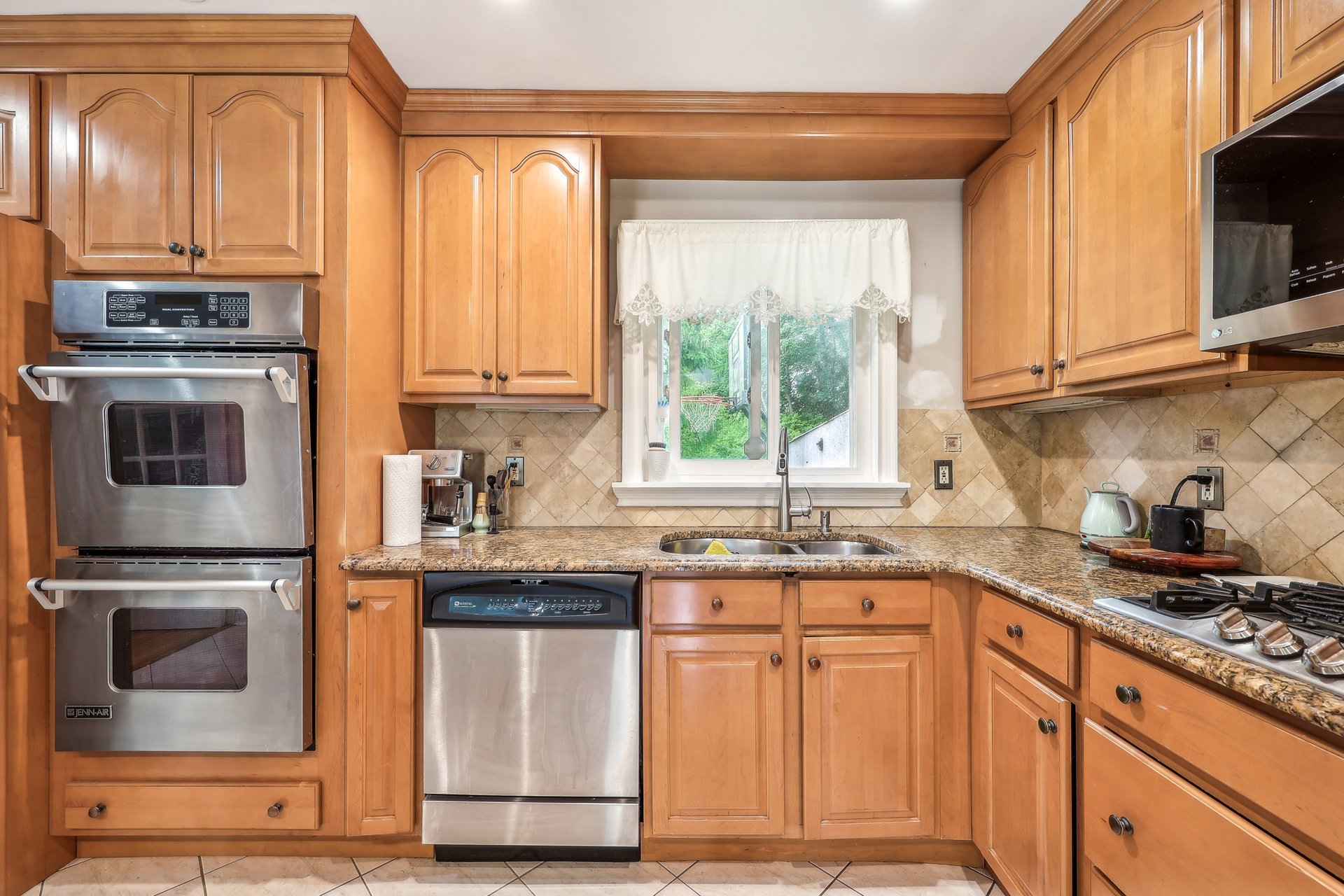 Kitchen with warm wood cabinetry, granite counters, stainless steel appliances, and a sink beneath the window.