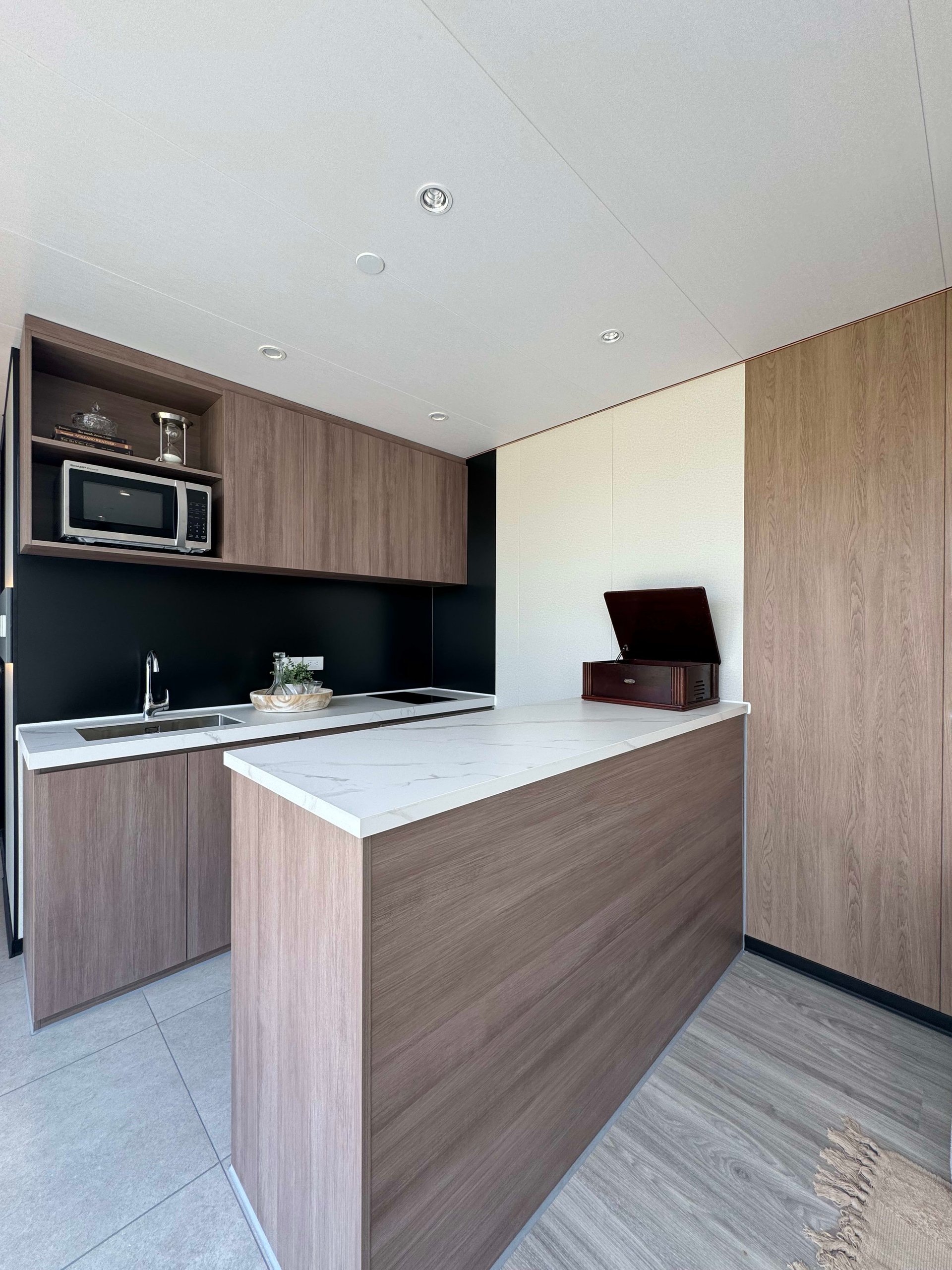 Compact kitchen with a white stone island, wood cabinetry, black backsplash, and built-in microwave.
