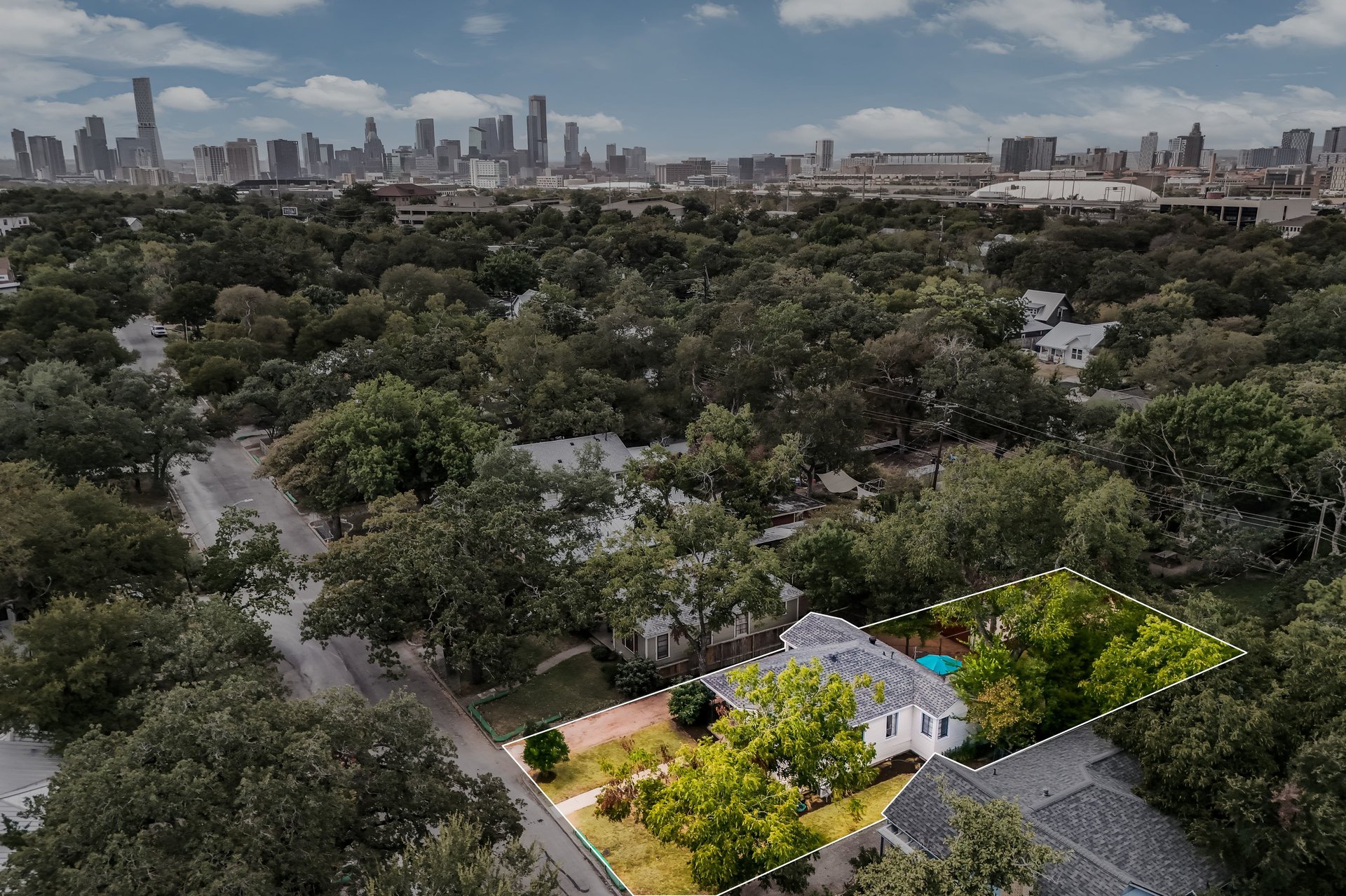 Aerial view of a tree-lined home and backyard pool, with the Austin skyline in the distance.