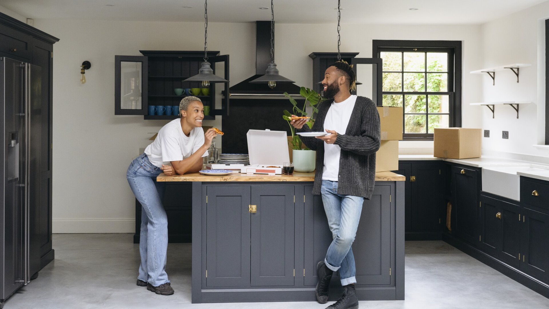 Two people eating together in a modern kitchen as they unpack moving boxes.