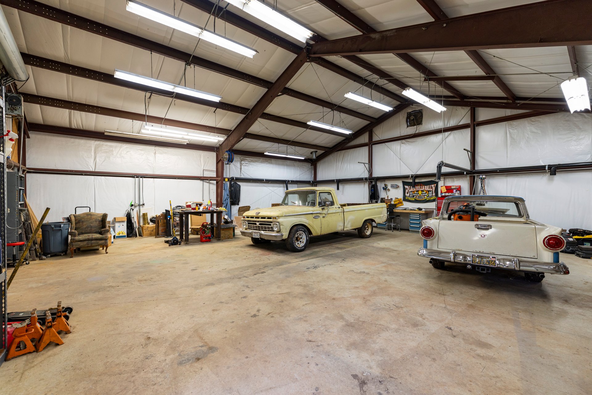 Large workshop with exposed steel beams, concrete floor, and two vintage pickup trucks.