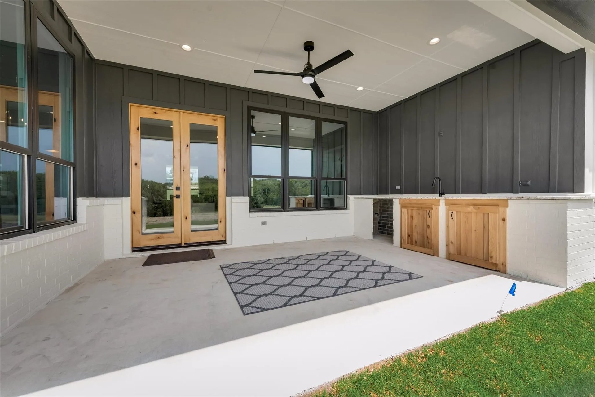 Covered patio with an outdoor kitchen, wood cabinets, glass doors, and a ceiling fan.
