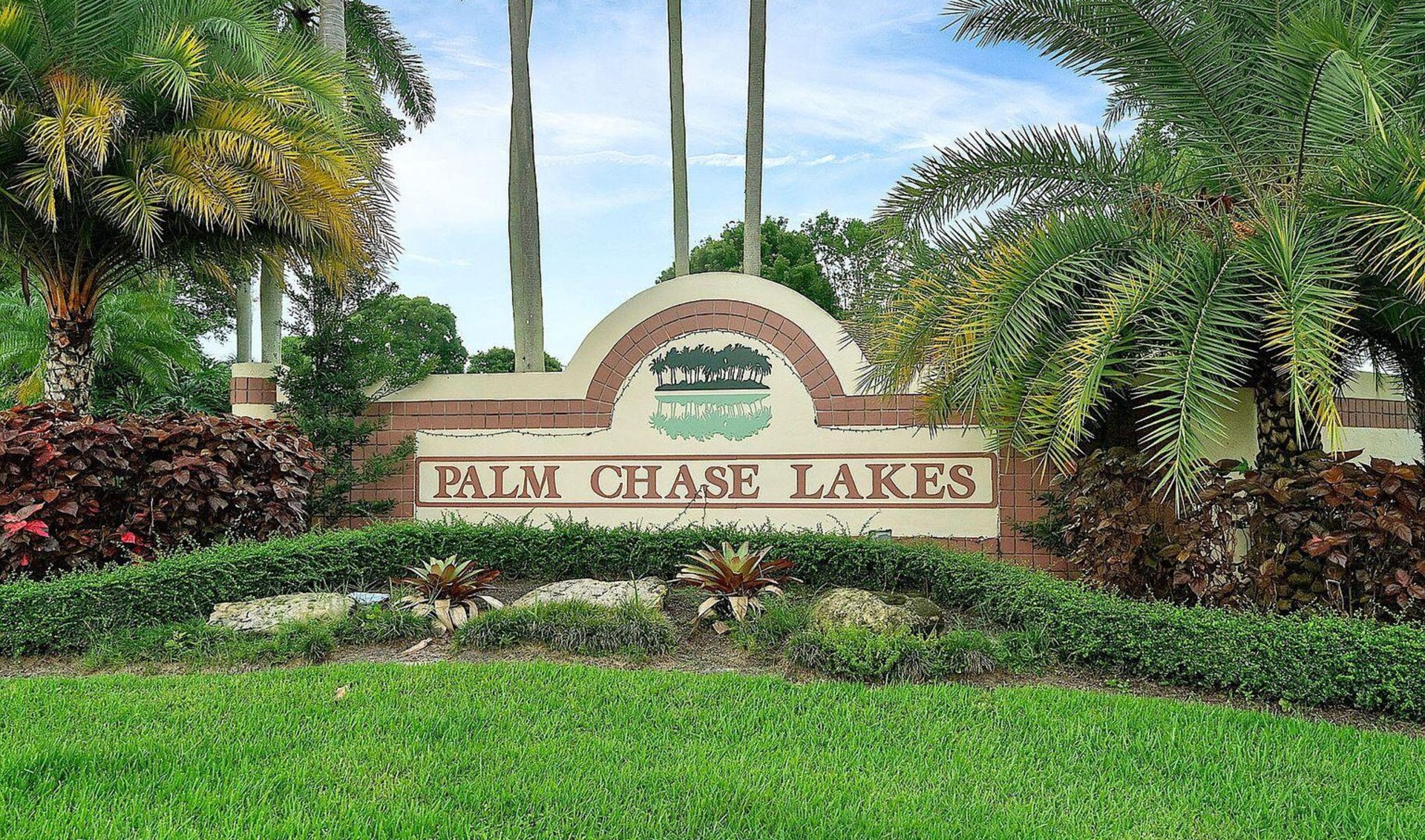 Palm Chase Lakes community entrance sign framed by palms and tropical landscaping.