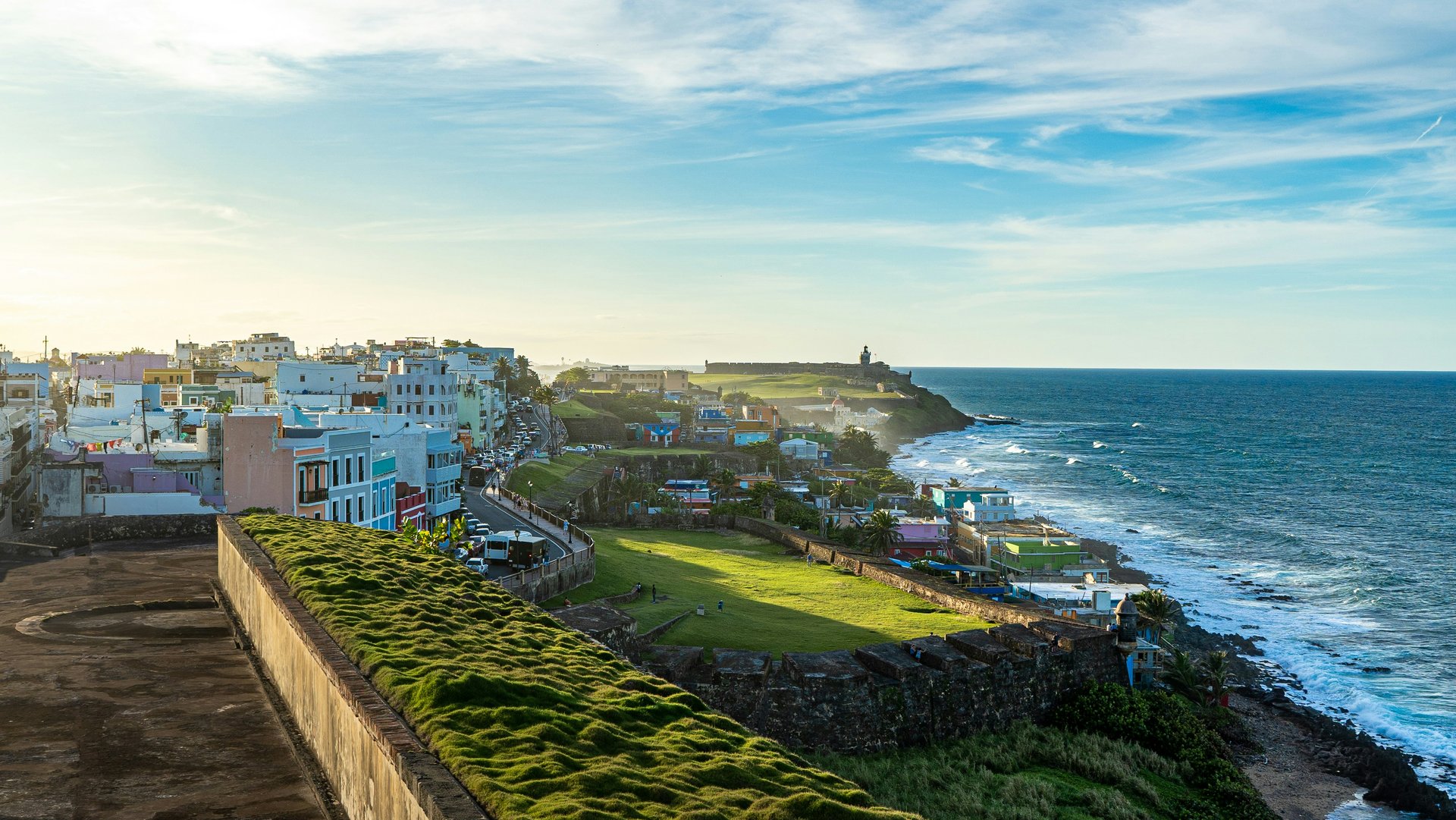 Coastal view of Old San Juan, Puerto Rico, featuring colorful buildings, a grassy fortification, and the Atlantic Ocean.