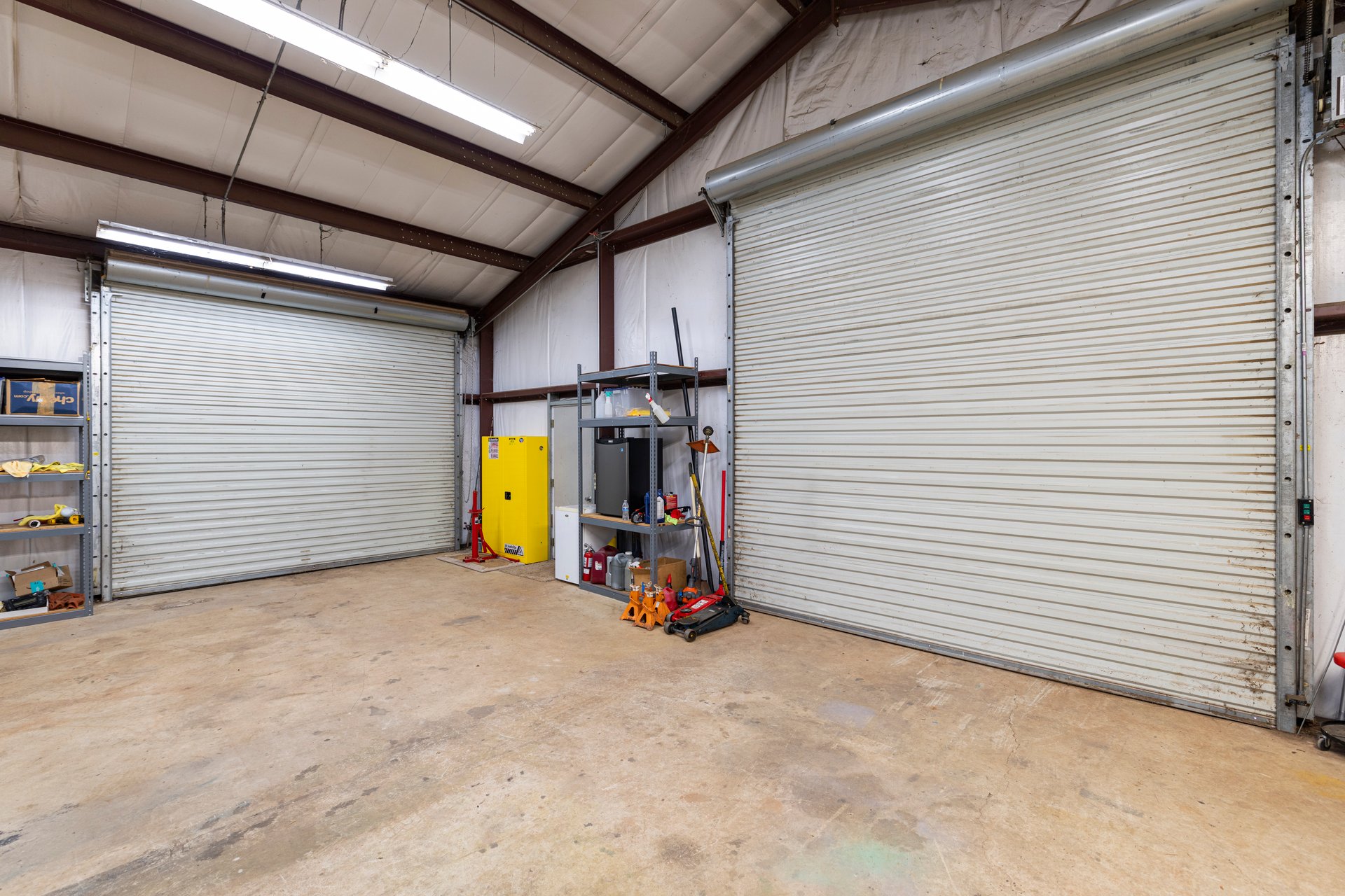 Garage workshop with two roll-up doors, exposed steel framing, and tool shelves.