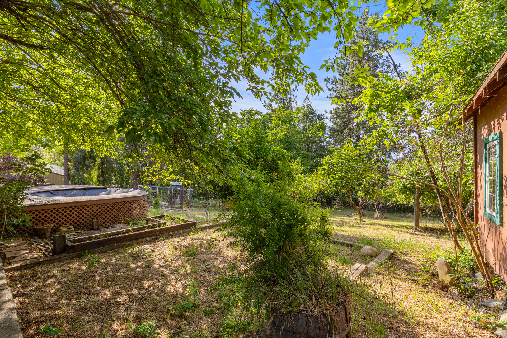 Leafy backyard with an above-ground hot tub, garden beds, and mature trees.