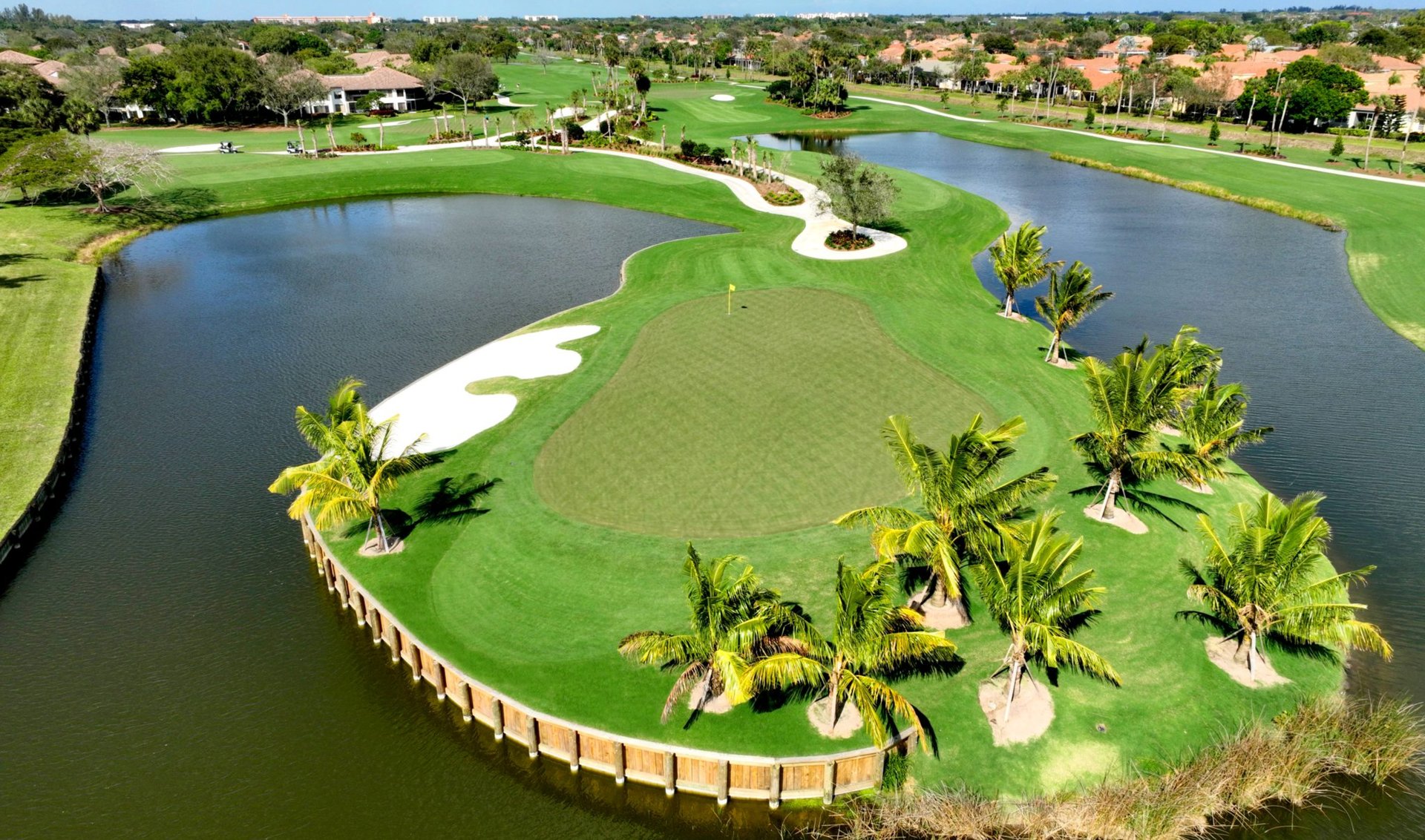 Aerial golf course with a palm-lined green, sand bunkers, and water hazards.