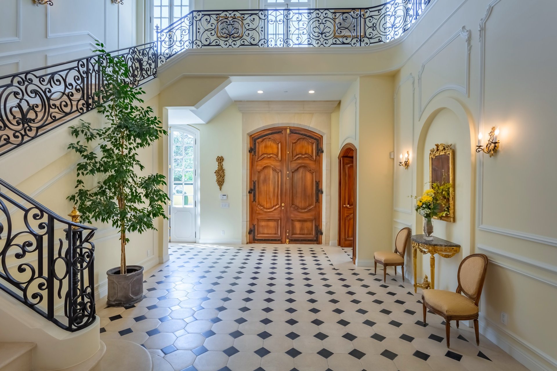 Grand foyer with wrought-iron staircase, carved double doors, and black-and-white tile floor.