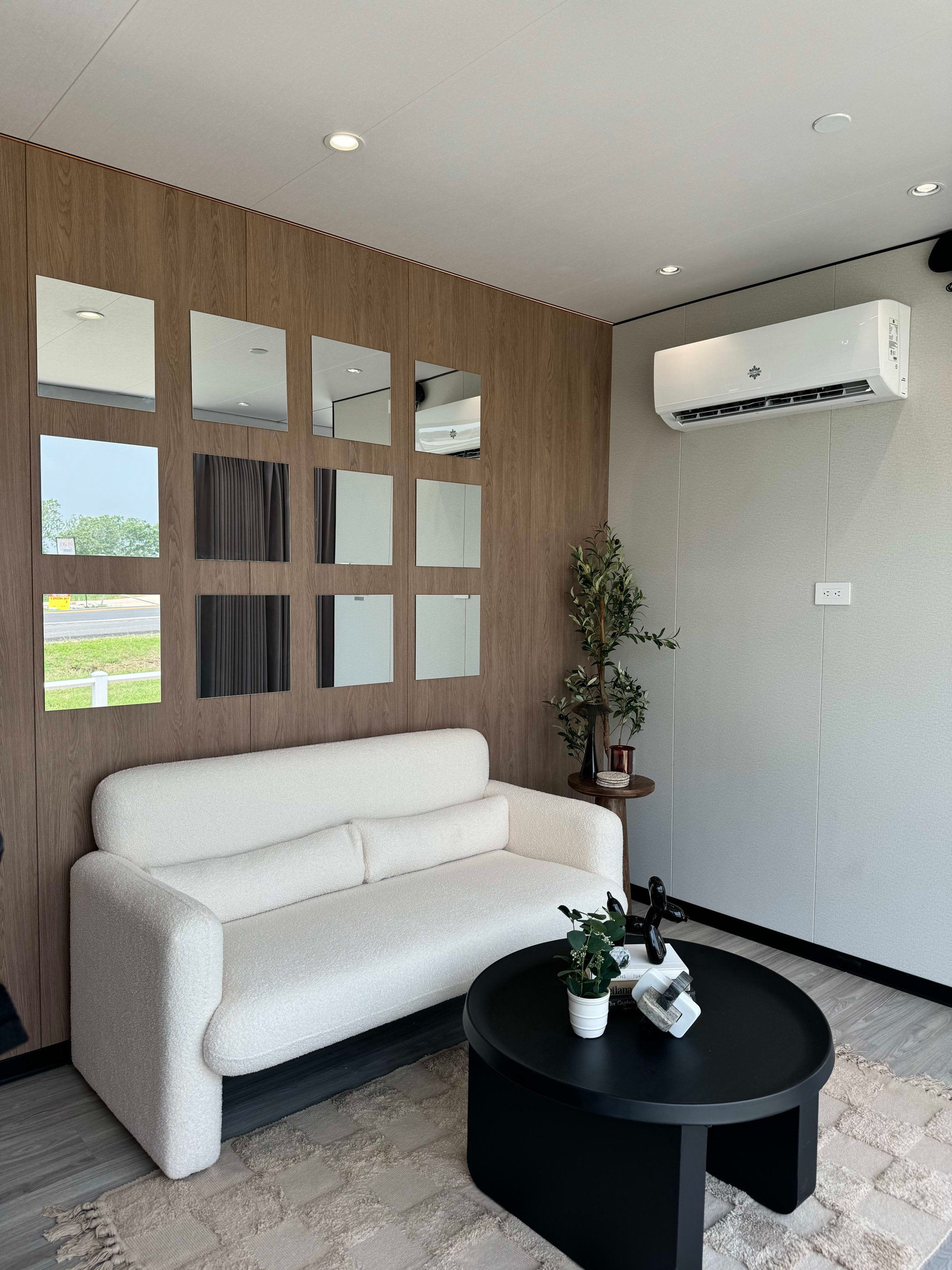 Tiny-home living room with a white sofa, round coffee table, and mirrored wood accent wall.