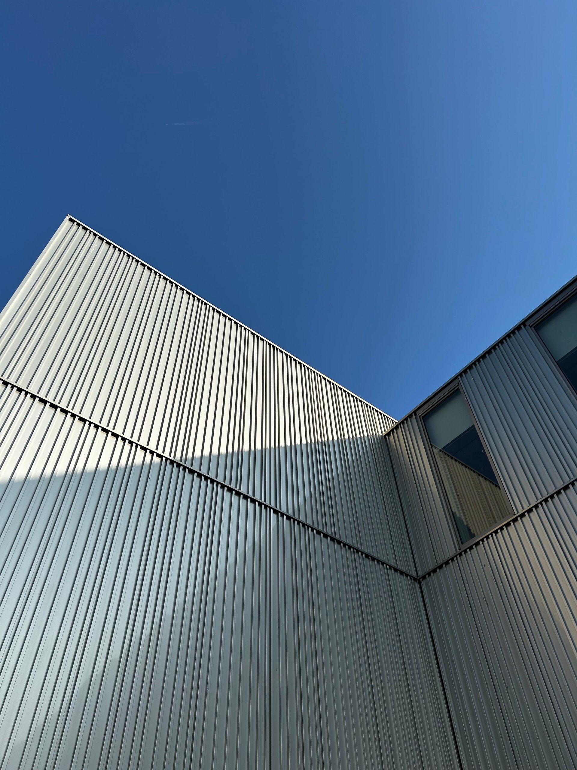 Modern industrial building with corrugated metal siding and dark windows against a blue sky.