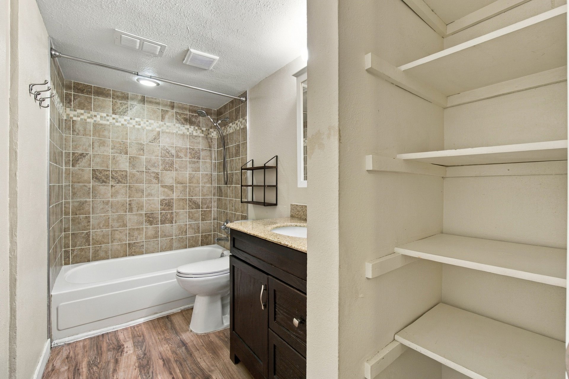 Bathroom with a tiled tub and shower, dark wood vanity, and built-in open shelving.